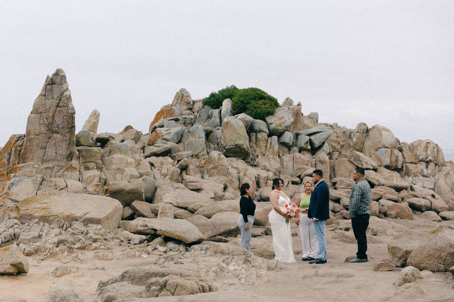 Small intimate wedding ceremony taking place among dramatic rocky coastal landscape.