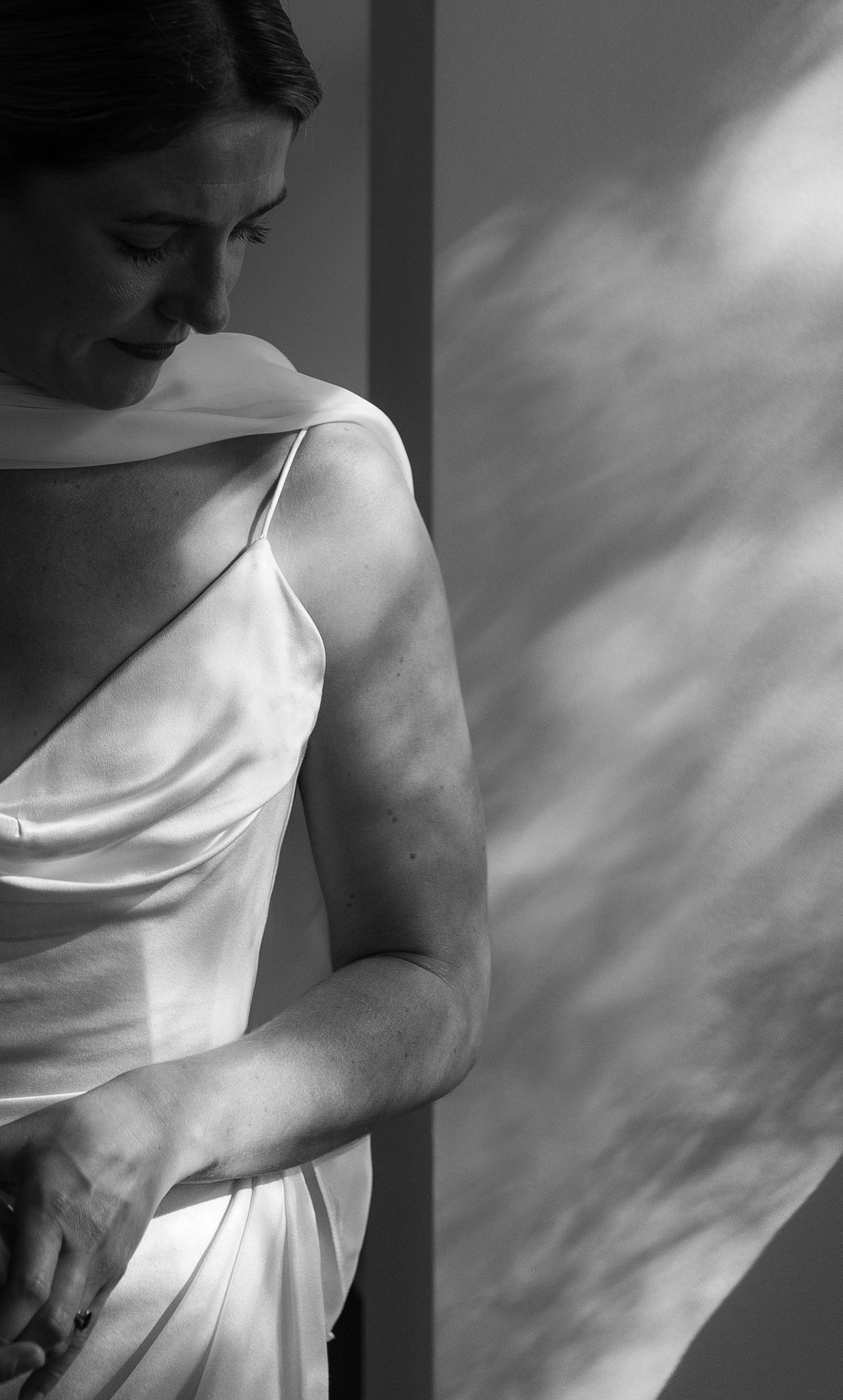 Black and white photo of a woman in an elegant satin slip dress, looking down with soft light casting shadows at Inn at the Presidio in SF.