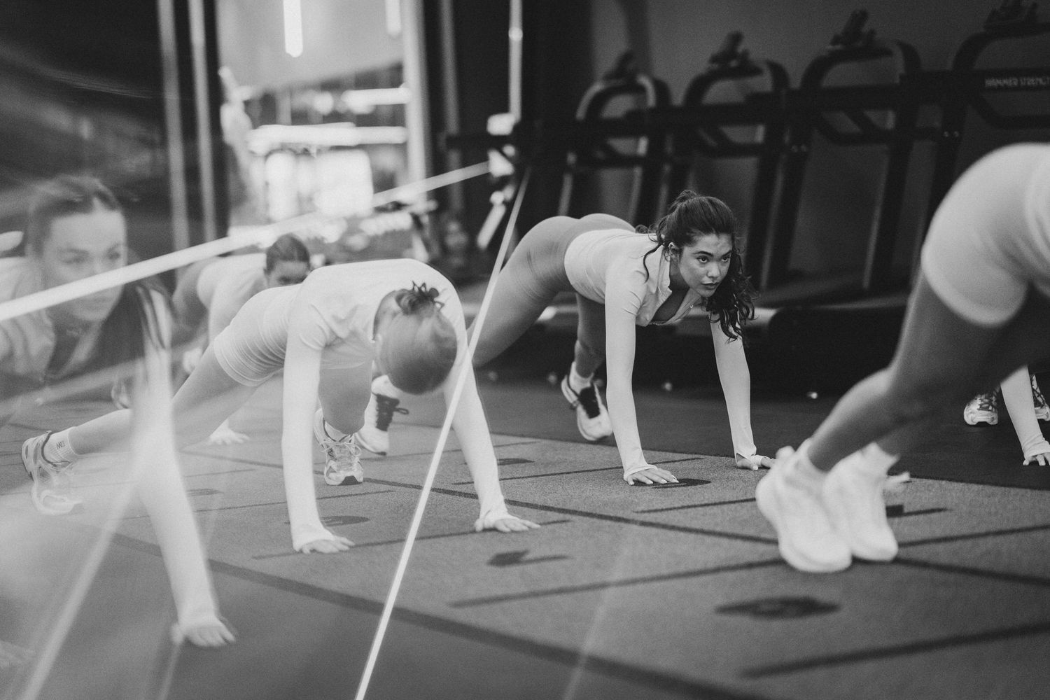 Women performing plank exercises during a fitness class in a dark gym, black and white photo.