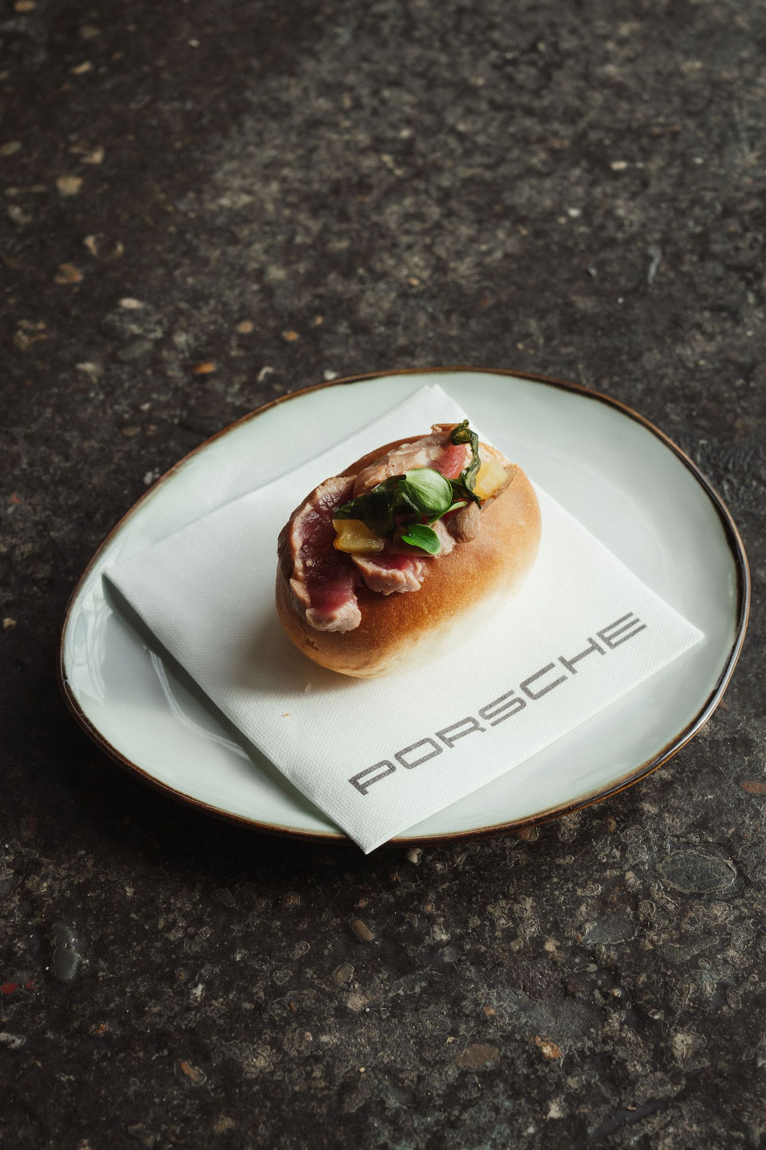 Gourmet sandwich on a Porsche branded napkin served on an elegant white plate with gold rim.