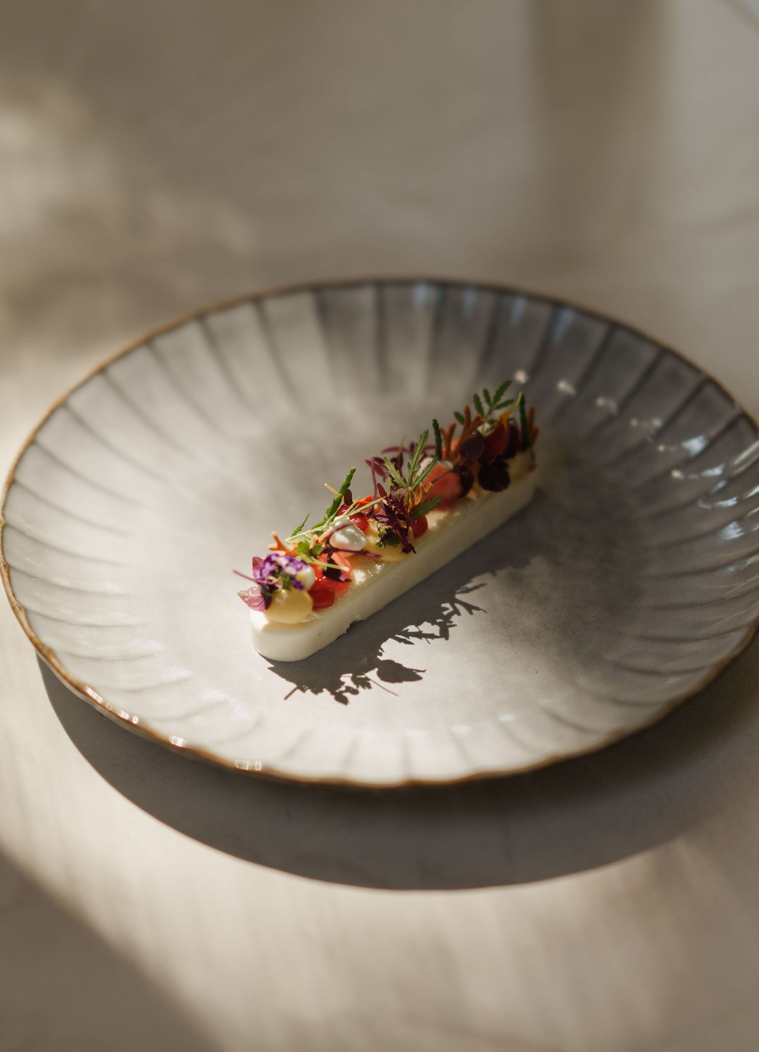 Elegant fine dining dish with edible flowers and microgreens on a rustic ceramic plate in soft natural light.