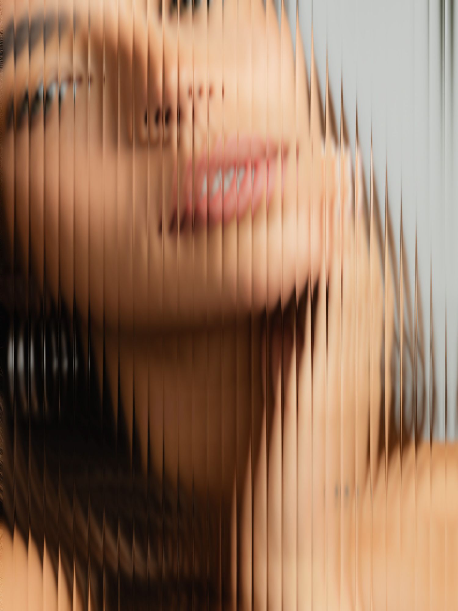 A smiling woman with dark hair viewed through textured ribbed glass creating a distorted abstract portrait effect.