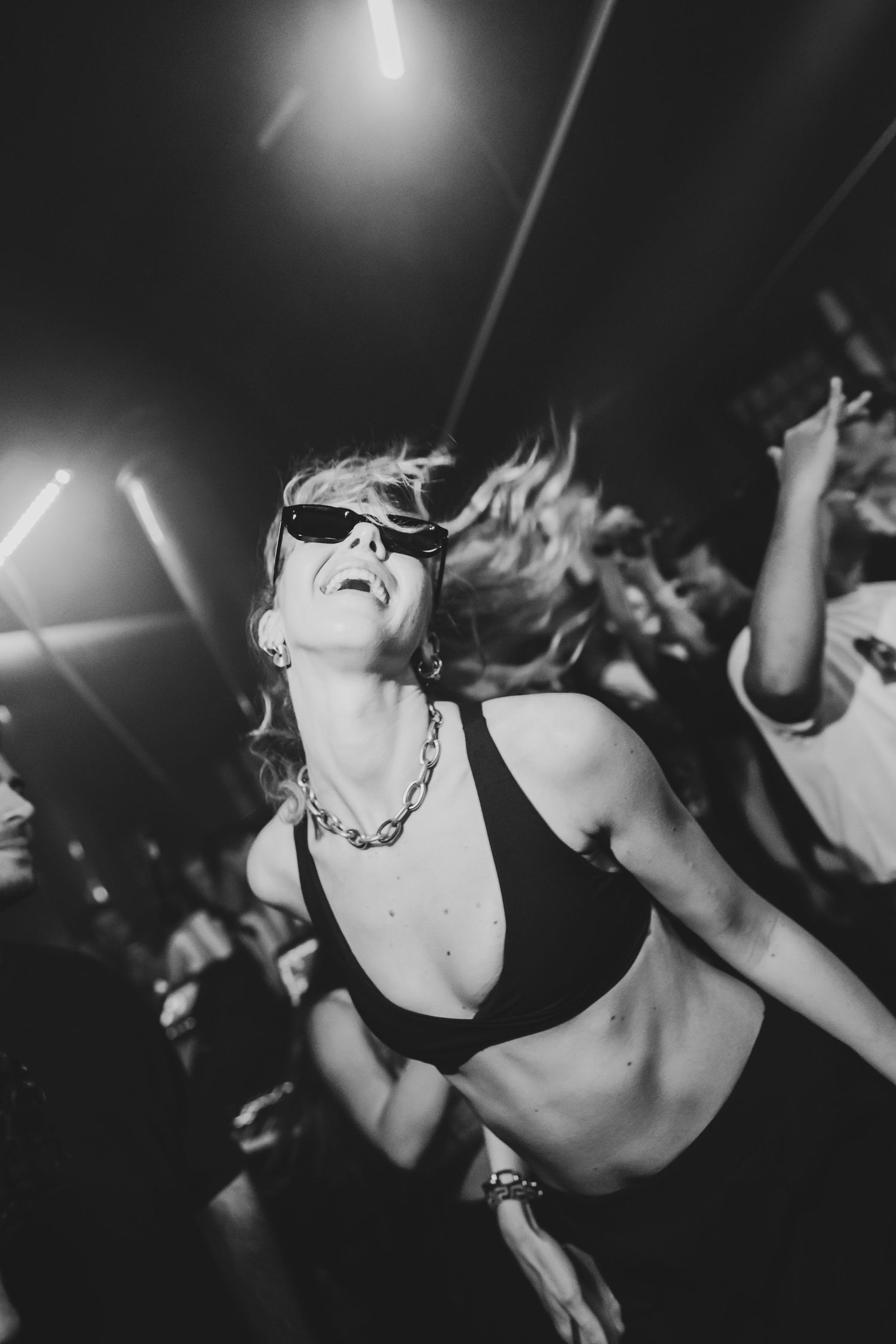 Black and white photo of a woman in sunglasses dancing energetically at a nightclub party.