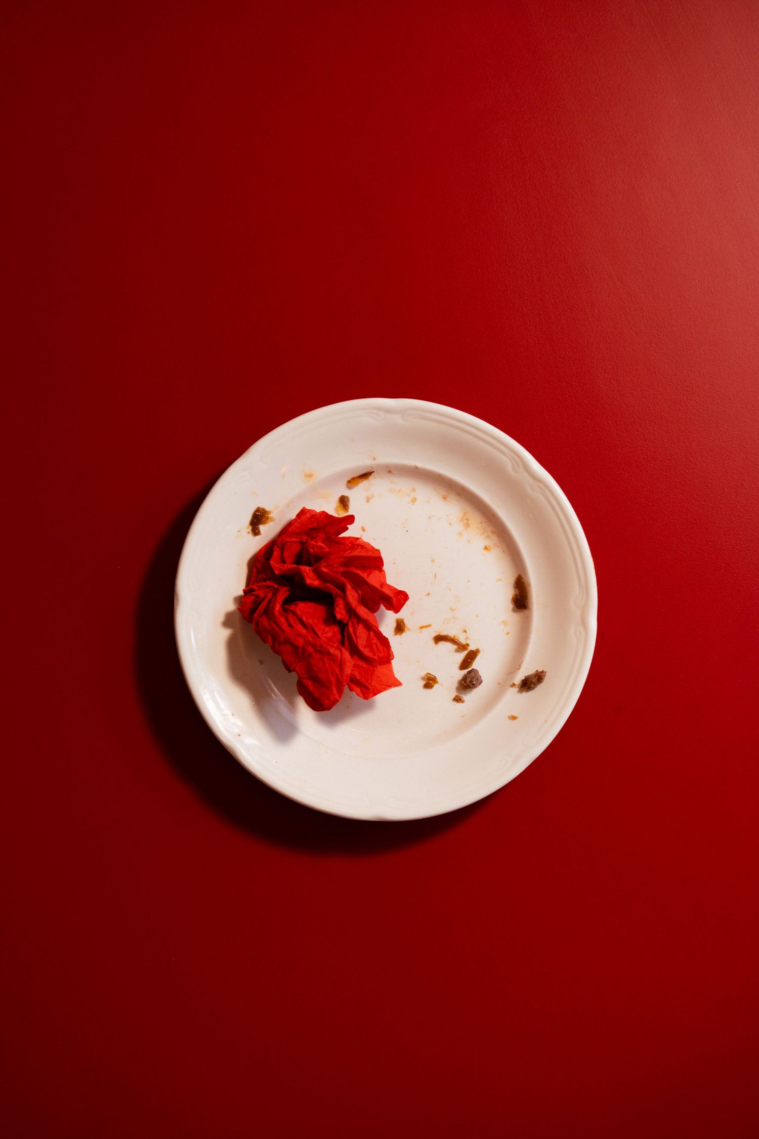 White plate with crumpled red napkin and crumbs on a red background.