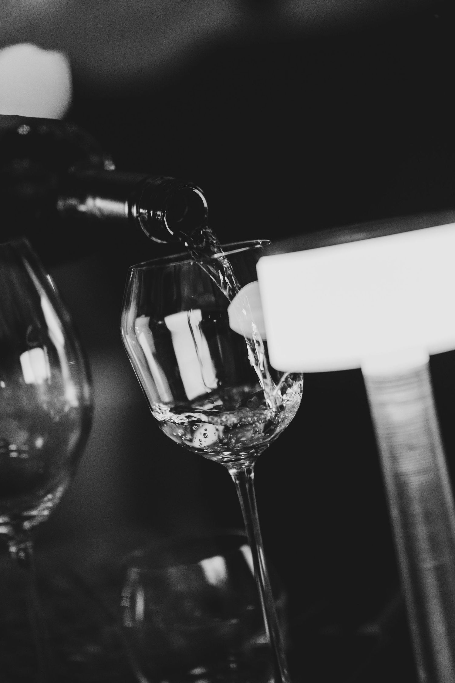 Black and white photo of wine being poured from bottle into elegant crystal wine glass at upscale event.