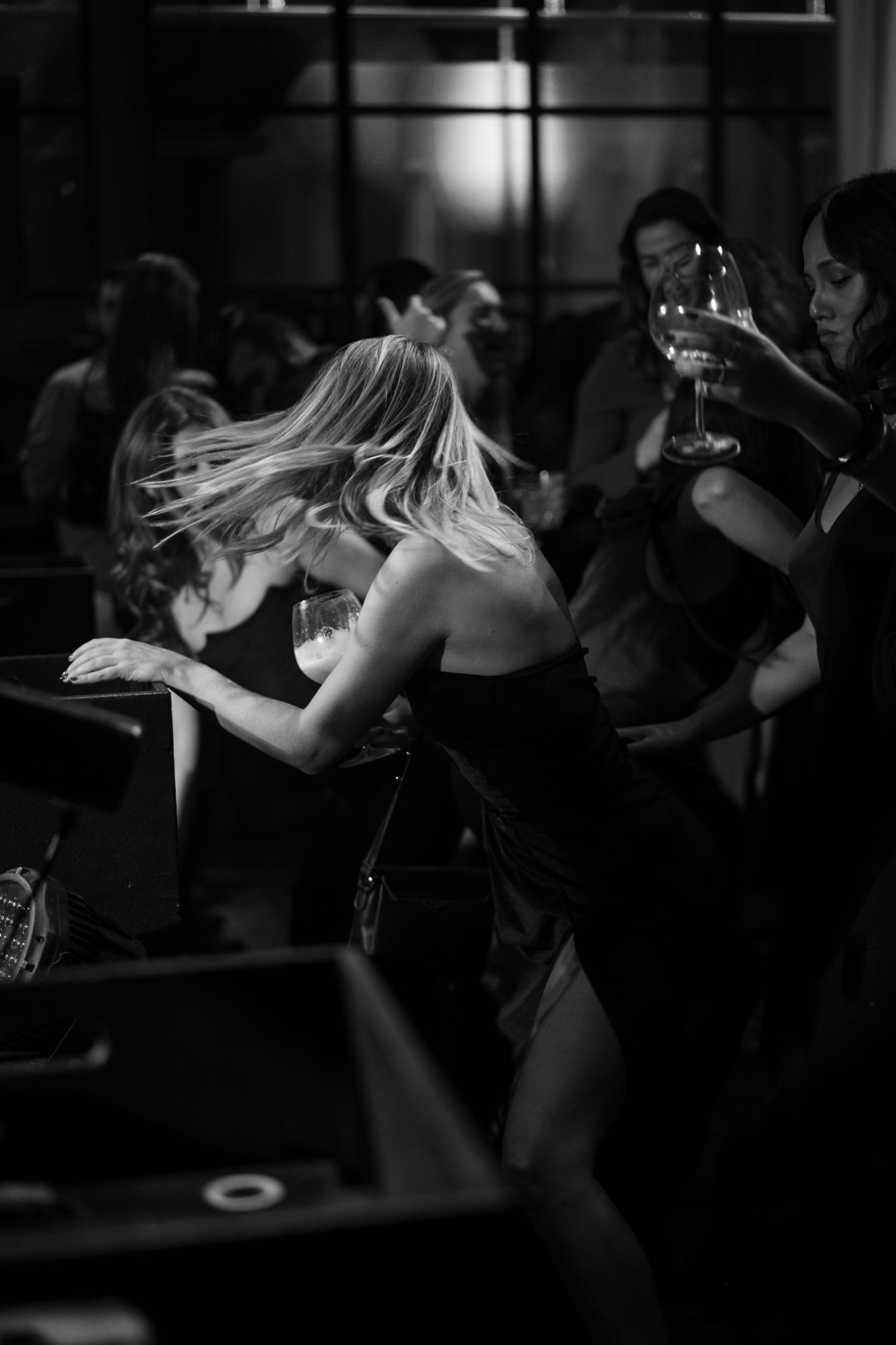 Black and white photo of a blonde woman dancing at an upscale party while others hold wine glasses.