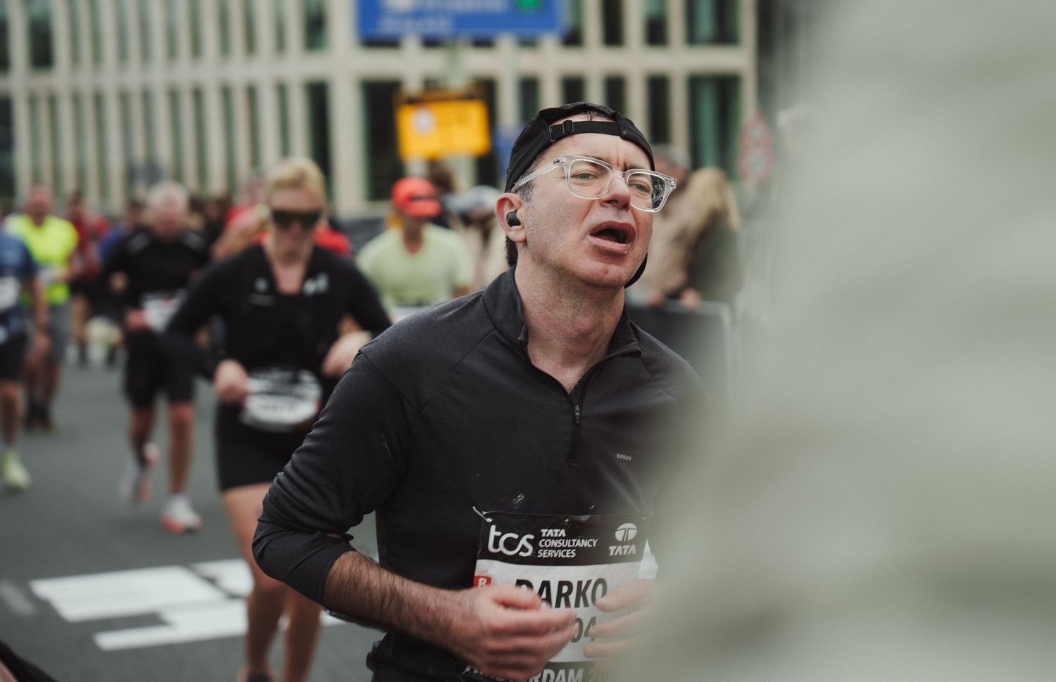 Marathon runner wearing glasses and black shirt exerts effort during urban race.