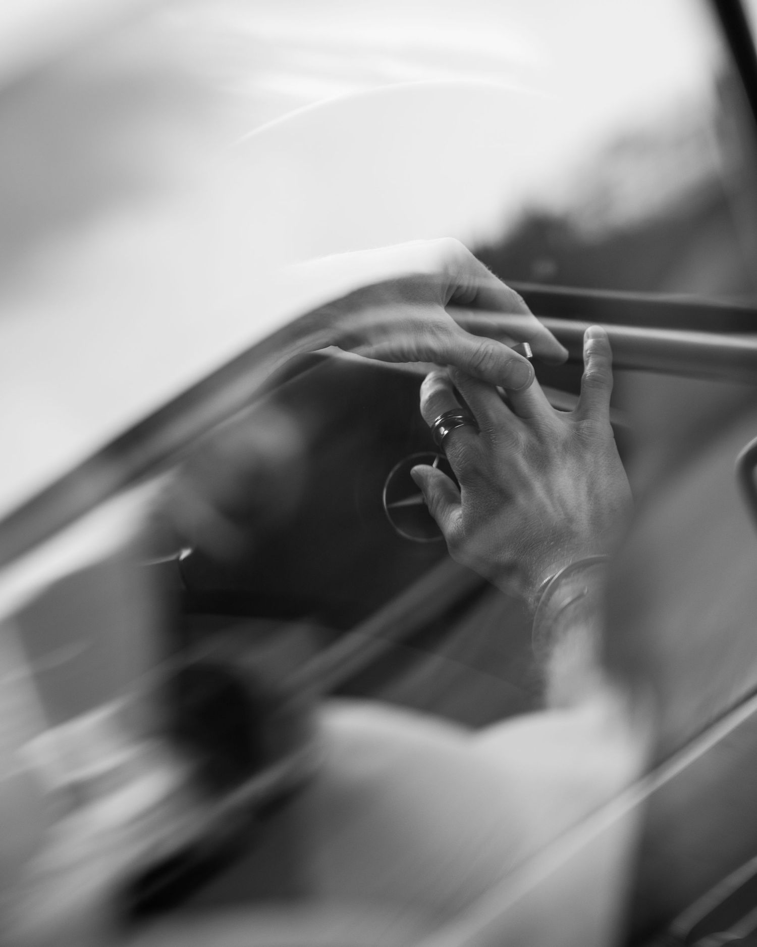 Black and white photo of hands gripping a car door frame, with a ring visible, captured in motion blur.