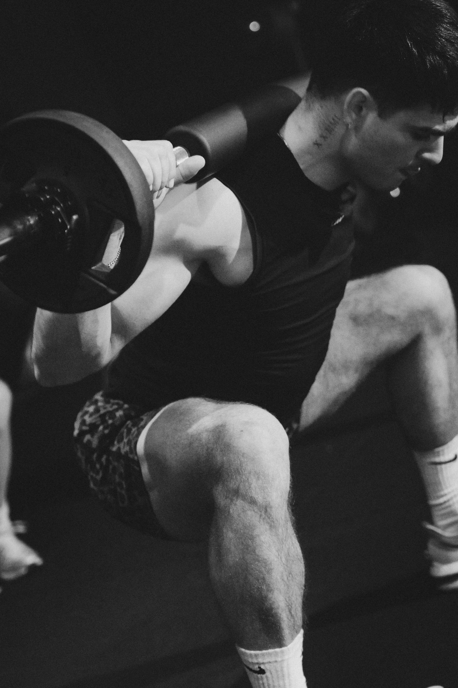 Muscular man performing barbell squats in a dark gym, black and white photo.