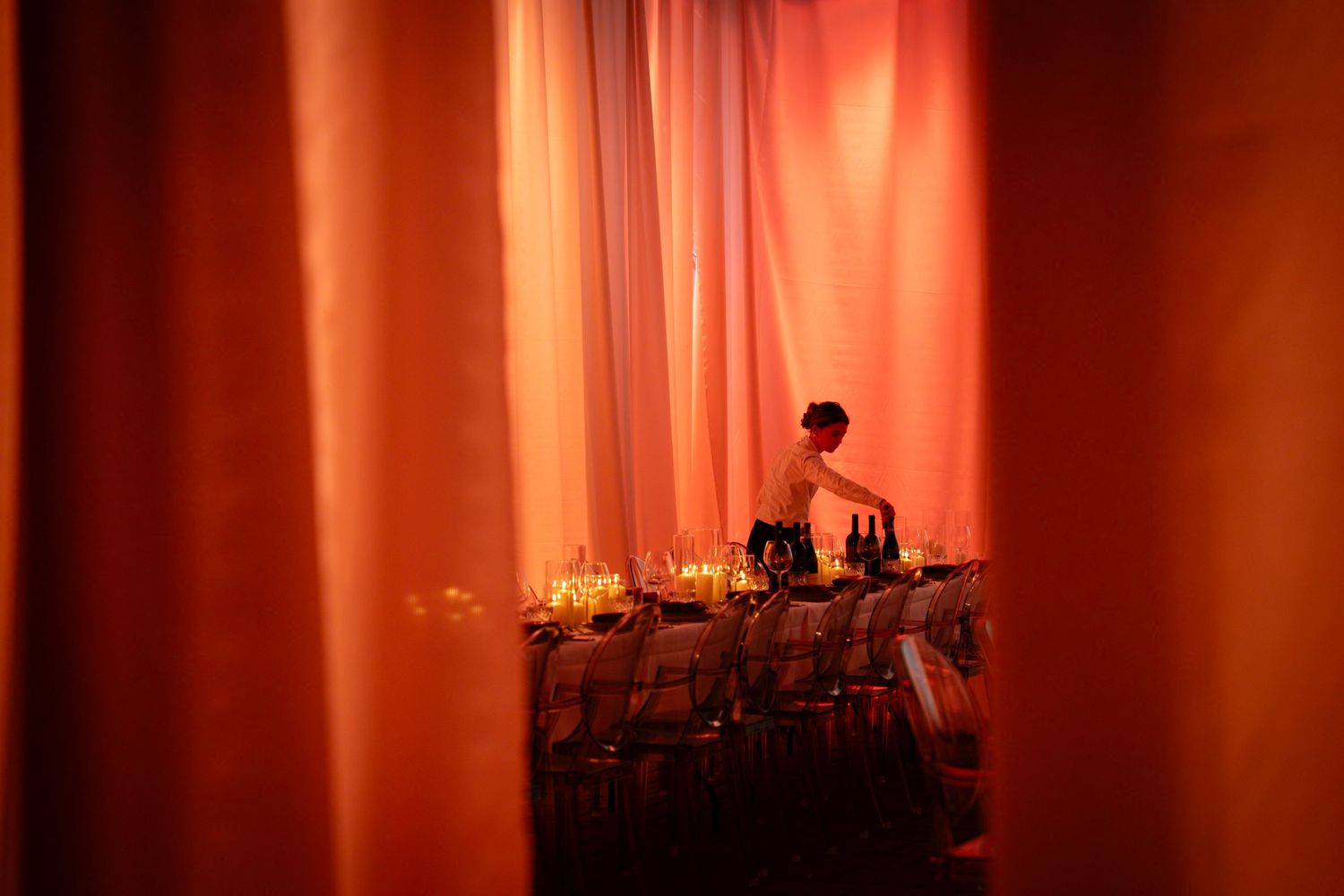 Bartender behind orange draped curtains serving drinks at an elegant event with warm amber lighting.