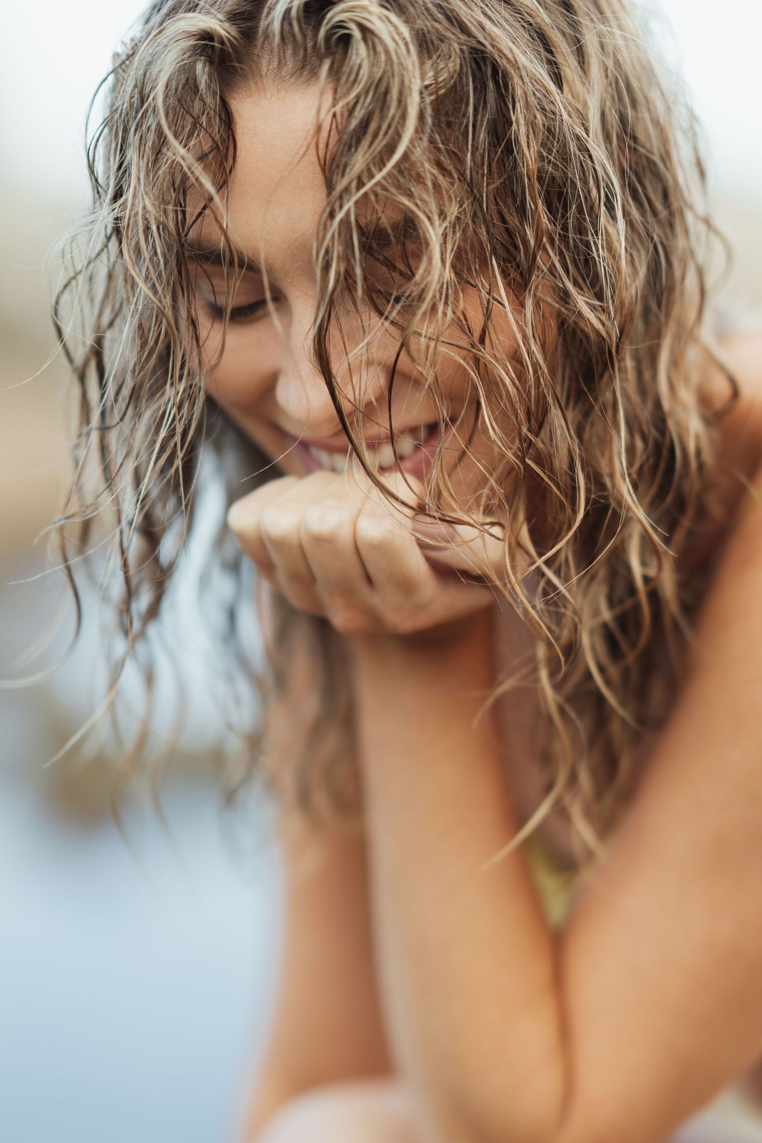 Smiling woman with wet curly hair resting chin on hand outdoors near water.
