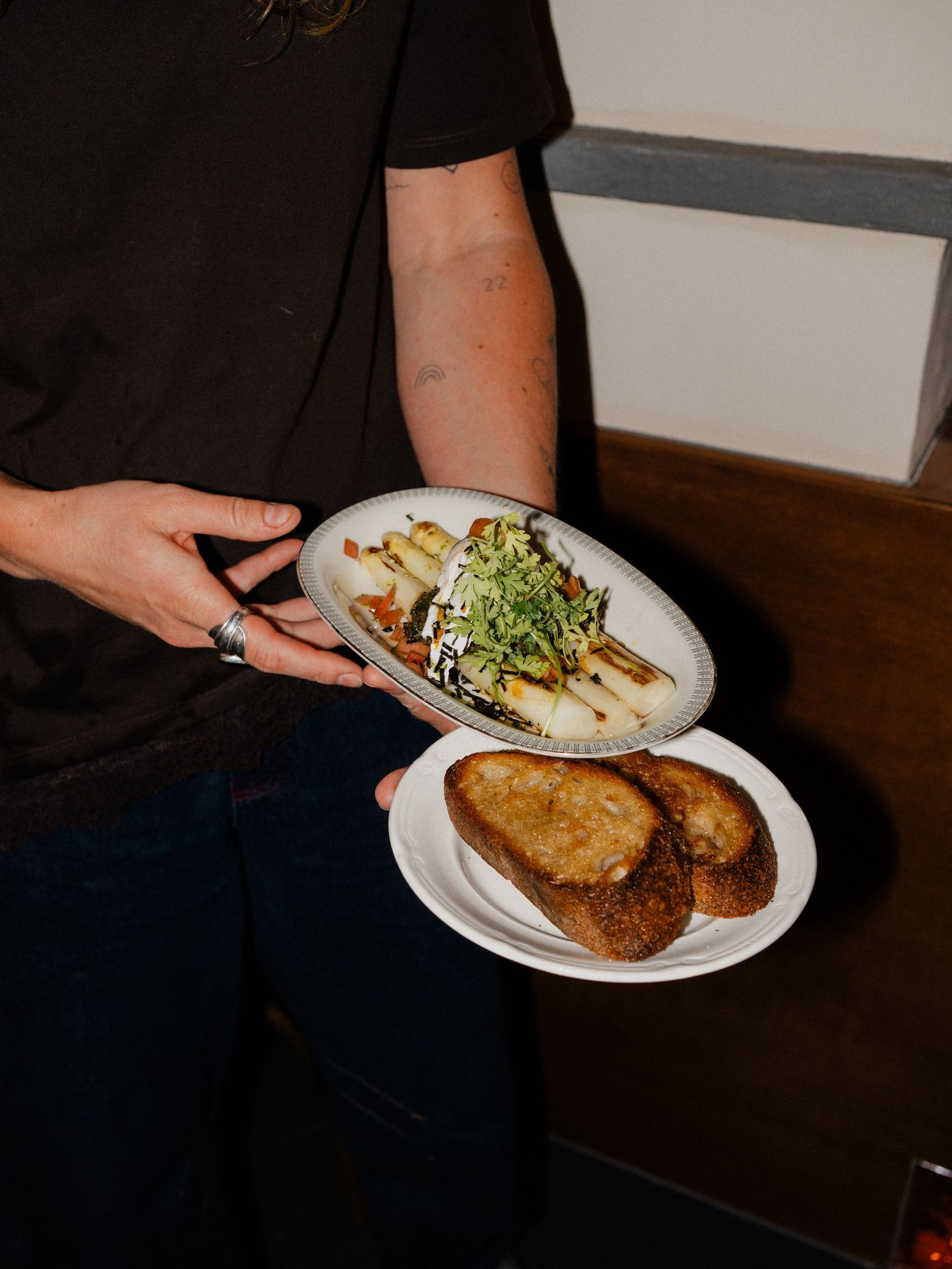 Server holding oval plate with salad and round plate with toasted bread slices.