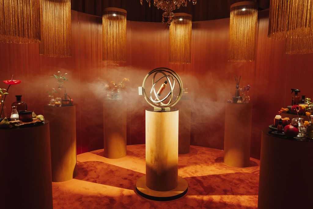 Luxurious golden room with a glowing armillary sphere centerpiece surrounded by pedestals displaying flowers and perfumes.