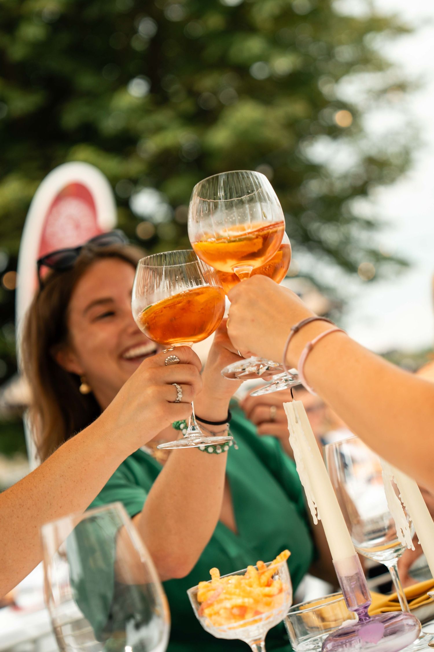 Women smiling and clinking glasses of Aperol Spritz at an outdoor summer party.
