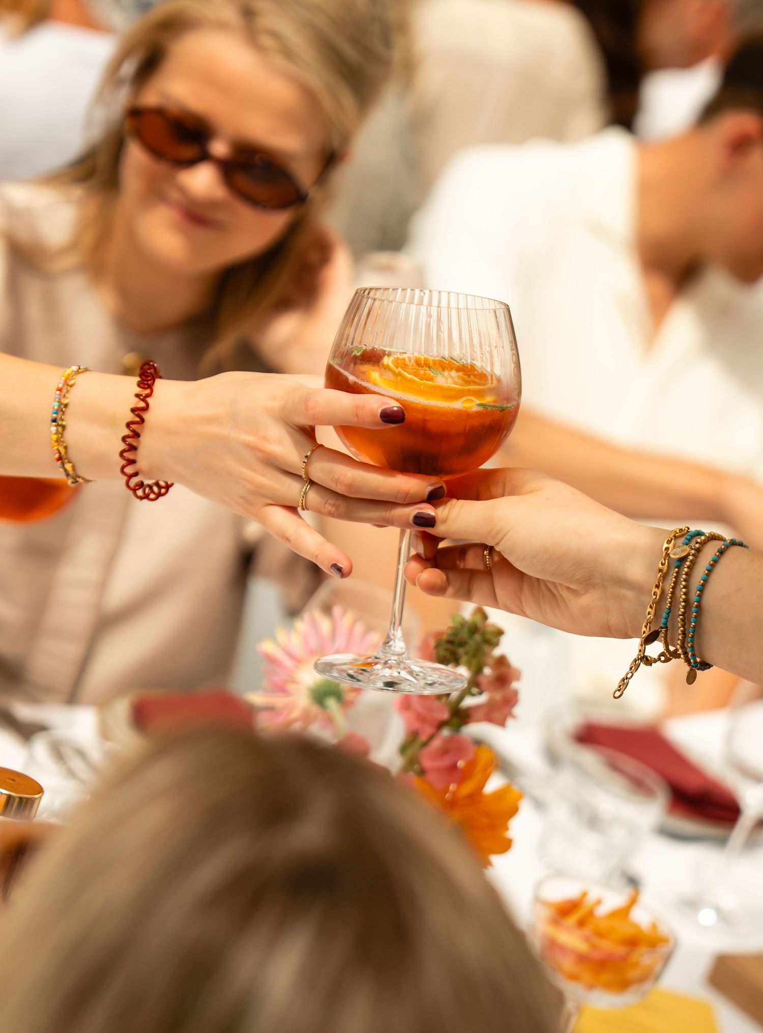 Women toasting with an Aperol spritz cocktail garnished with orange slice at an outdoor dining event.