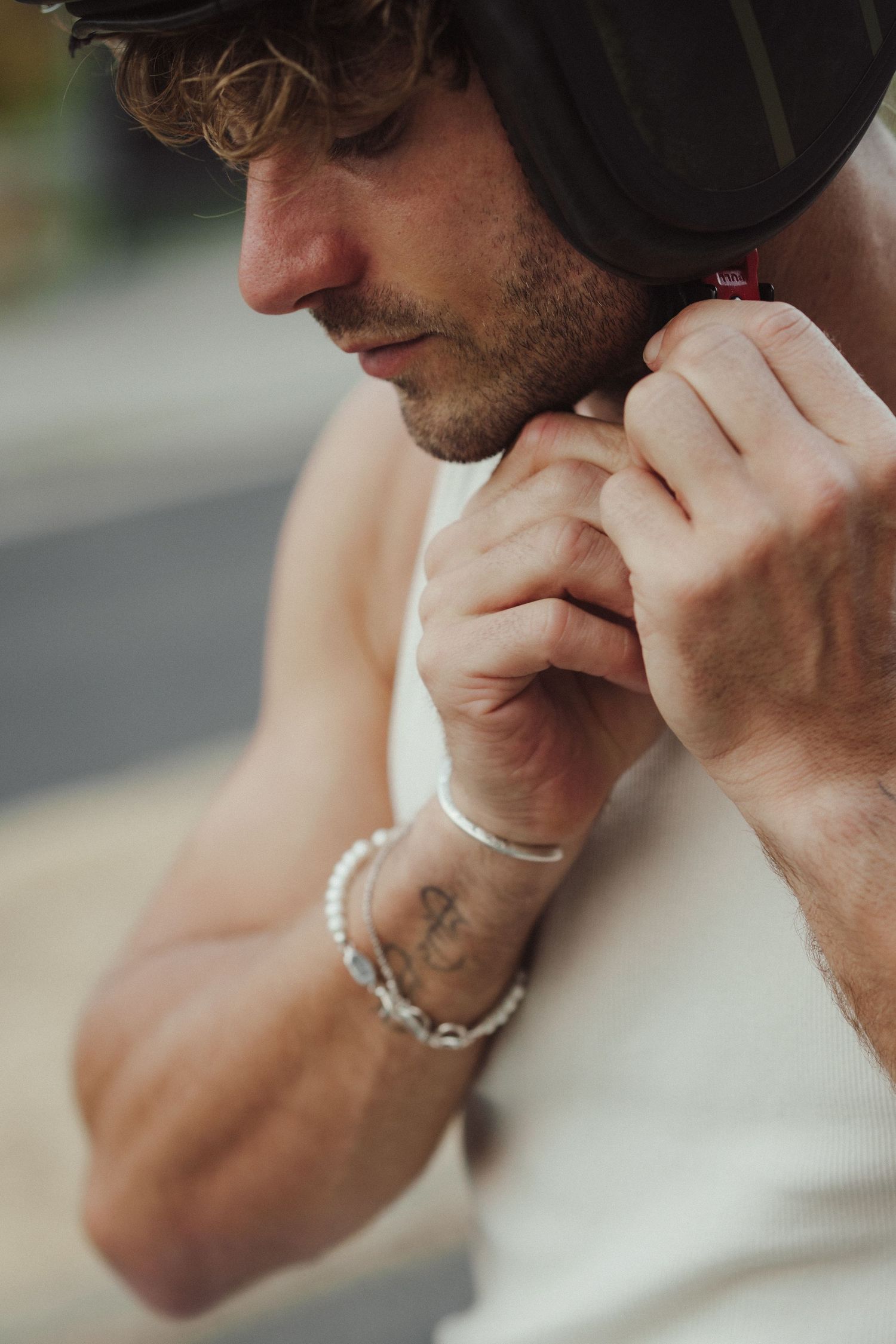 Man fastening a motorcycle helmet strap, wearing bracelets and a tattoo on his wrist, in a close-up shot.