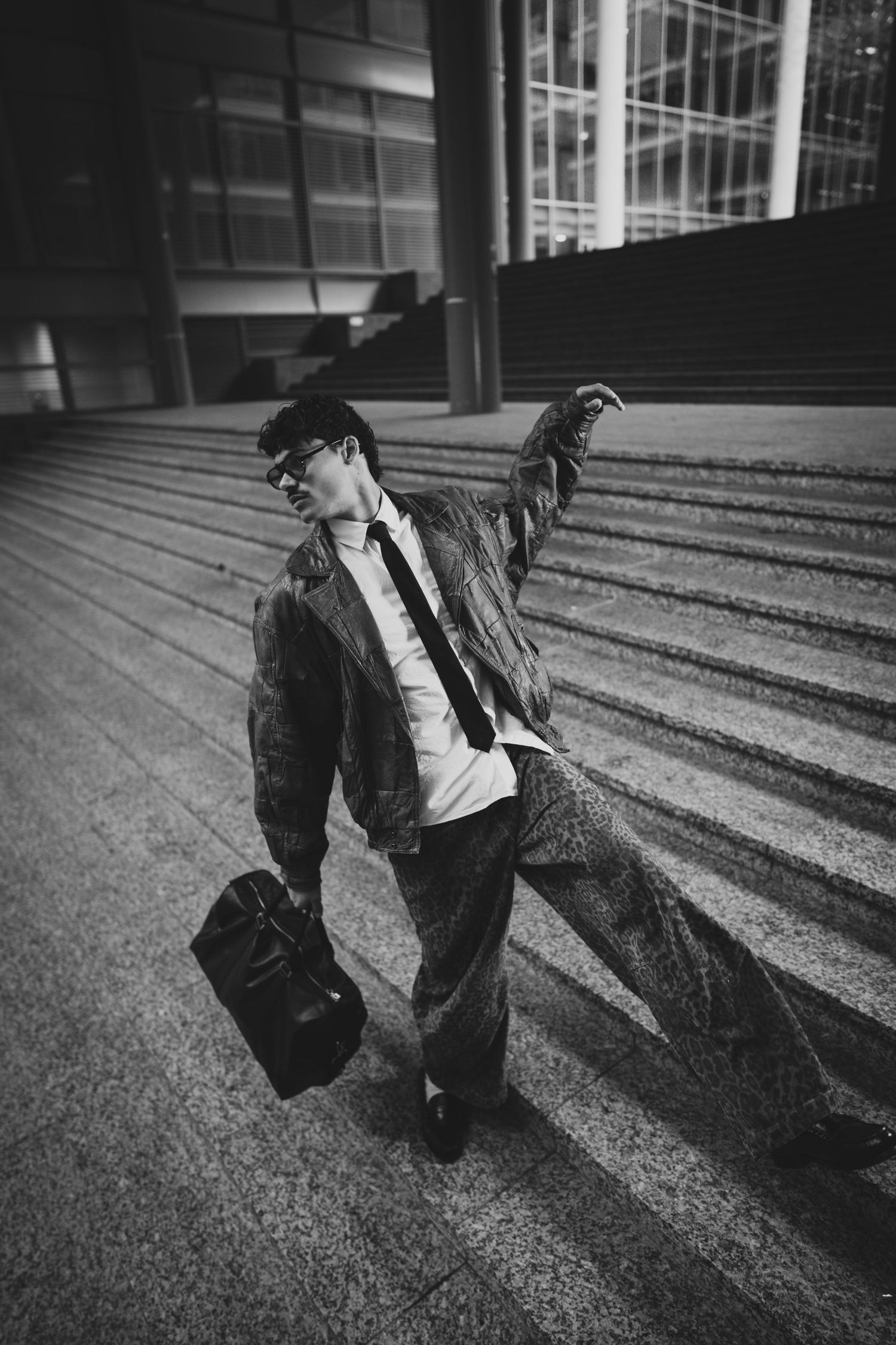 Black and white photo of a businessman in a suit carrying a briefcase, striking a dynamic pose on urban steps.