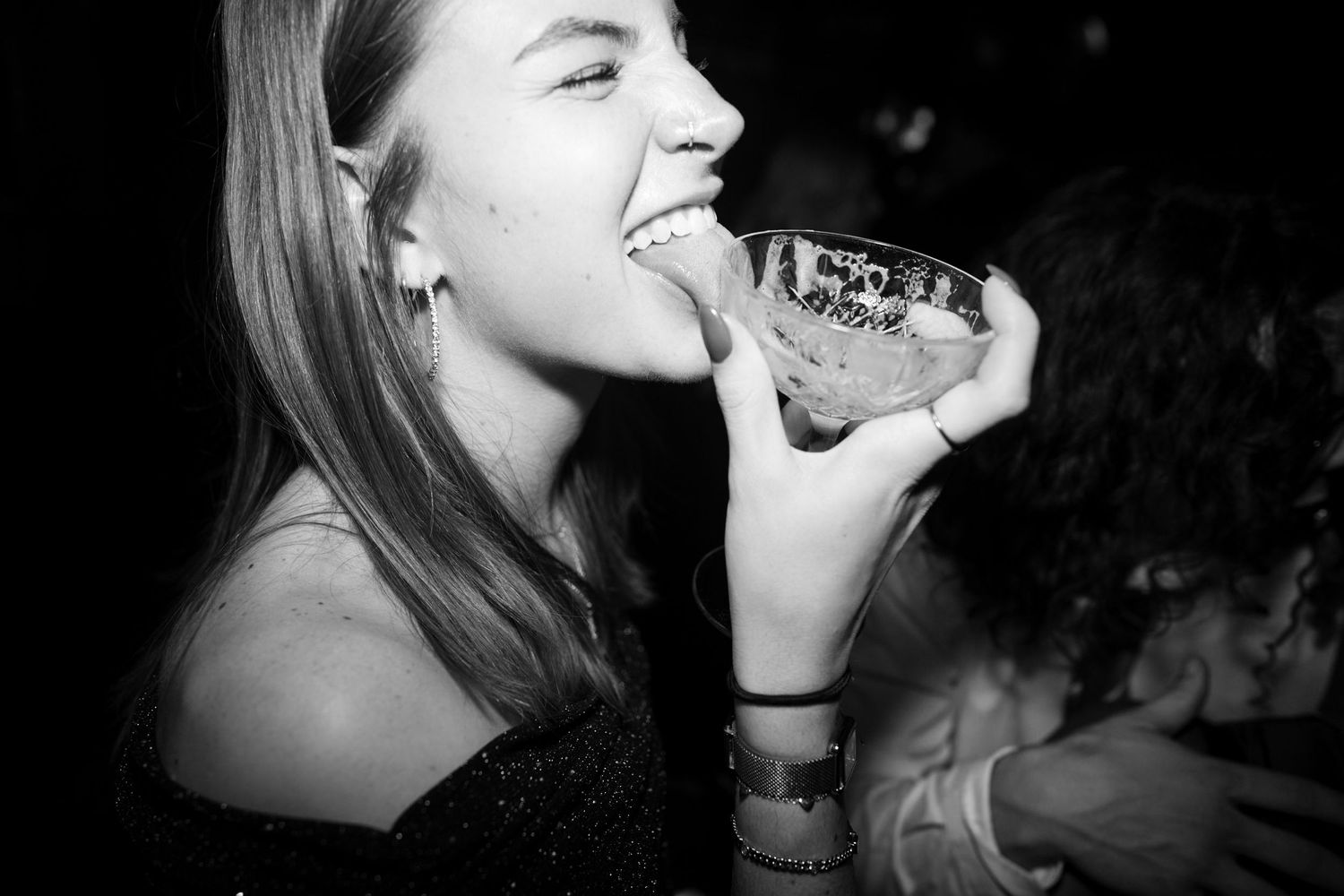 Young woman laughing and drinking from a glass at a nightclub party in black and white photo.