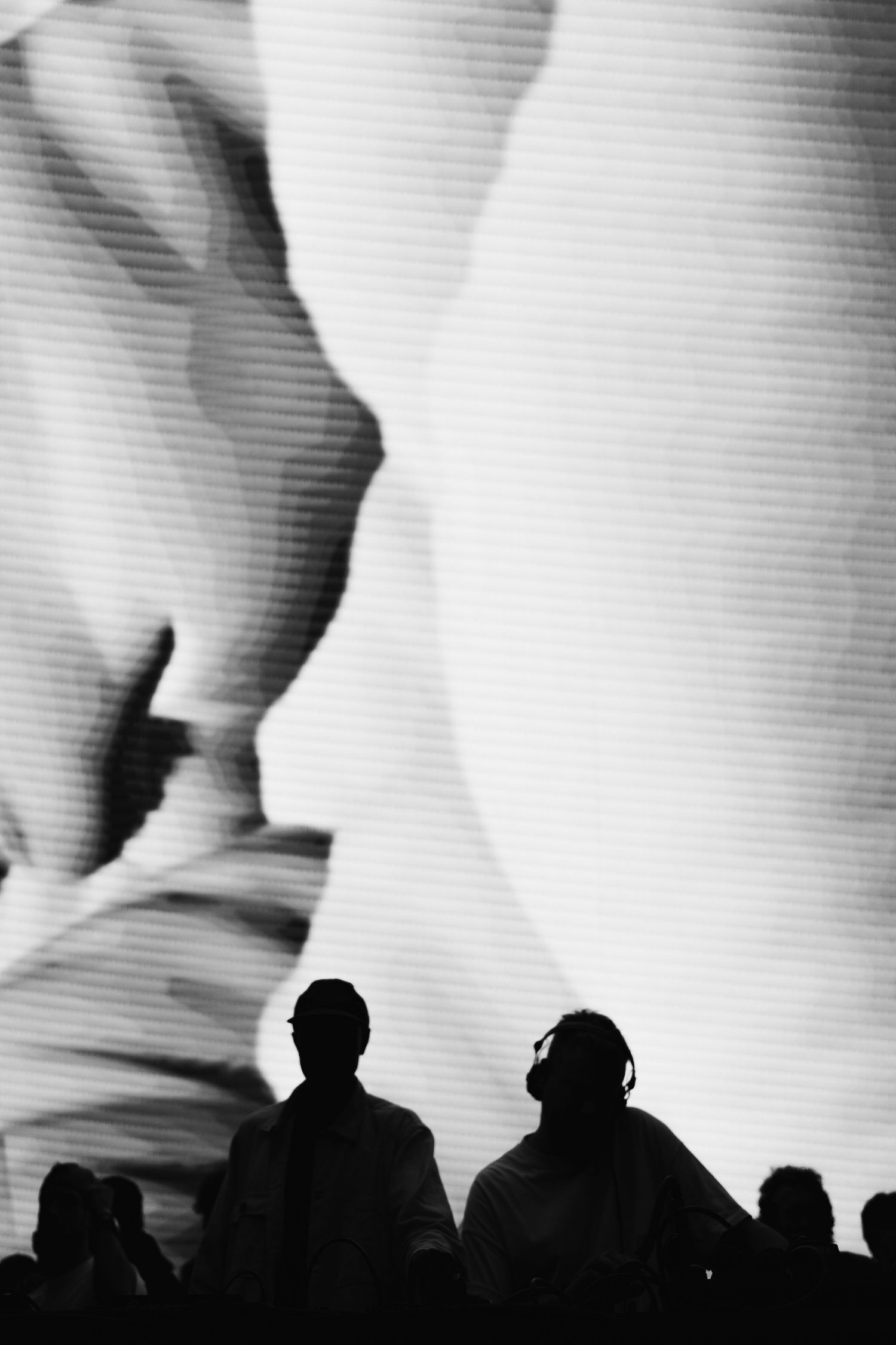 Silhouettes of people stand before a large black and white projected image of abstract curves in a dark venue.