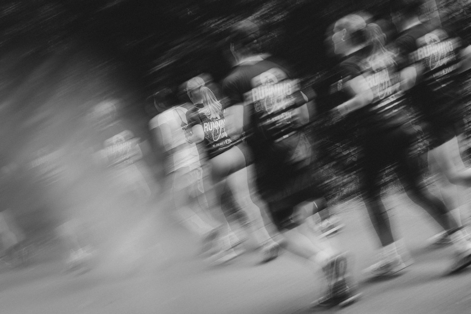 Blurred black and white photo of runners in motion during a race, capturing speed and energy.