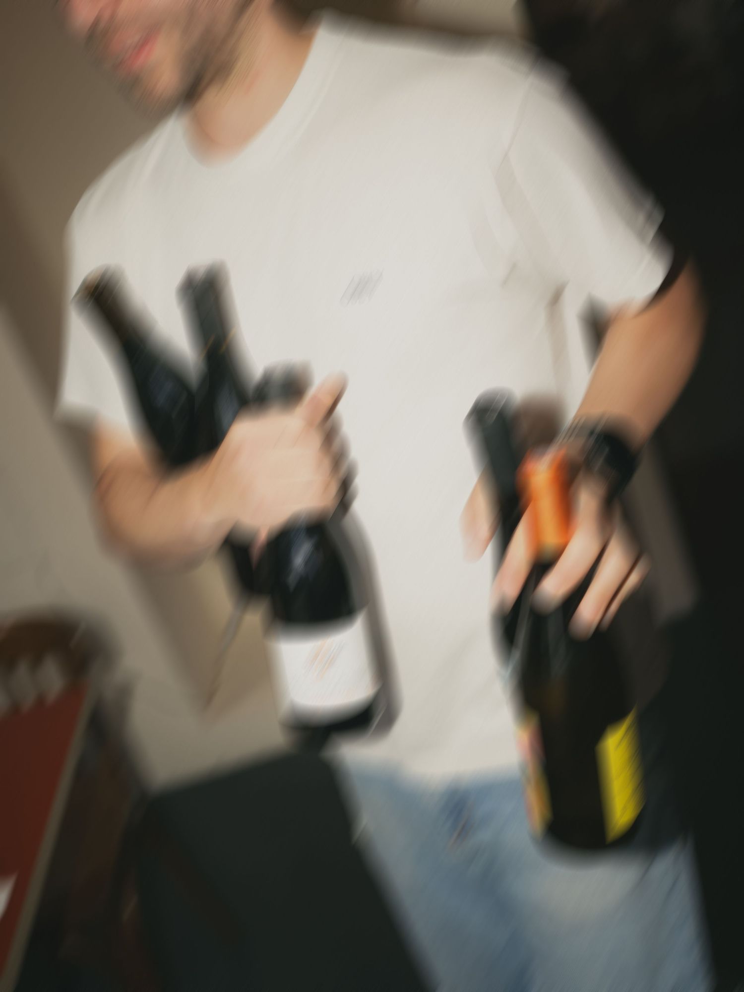 Man in white t-shirt holding multiple wine bottles at a party.