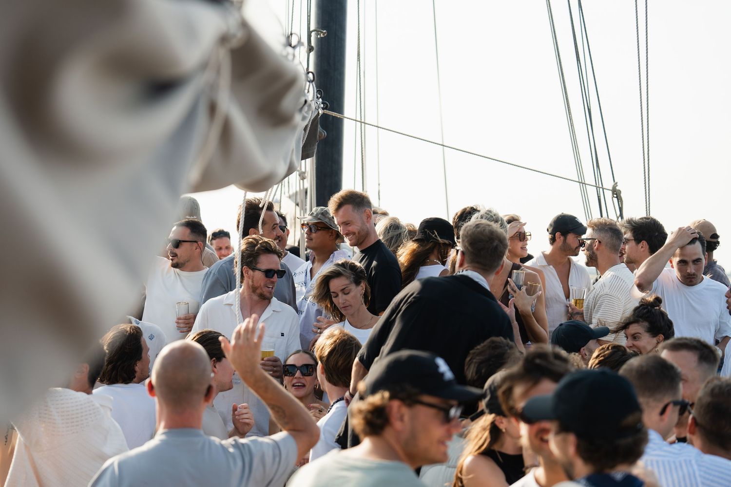 A large crowd of people dressed in white gather on a sailboat deck on a sunny day.