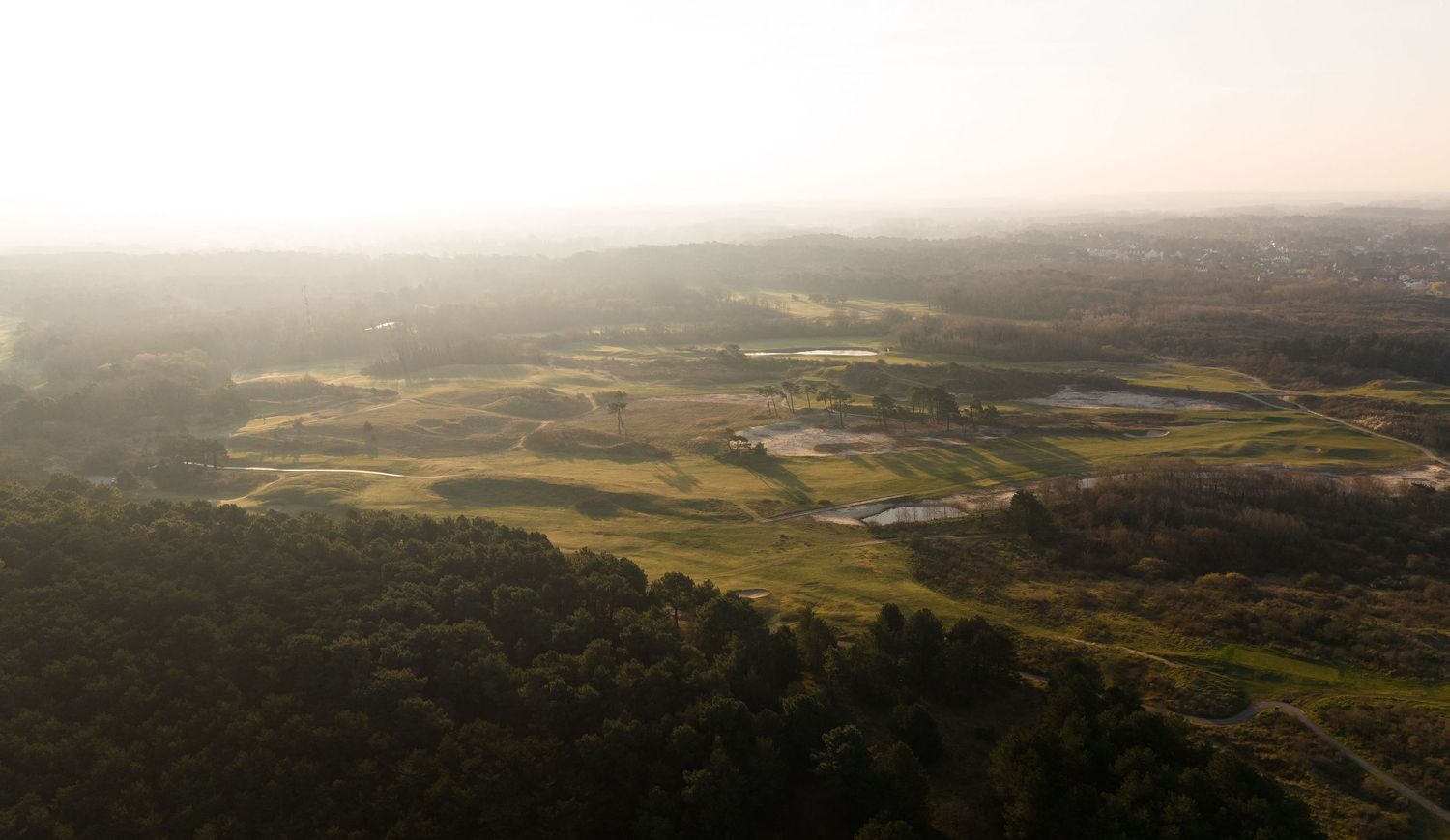 Aerial view of a lush green valley landscape with fields, trees, and misty hills in the background.