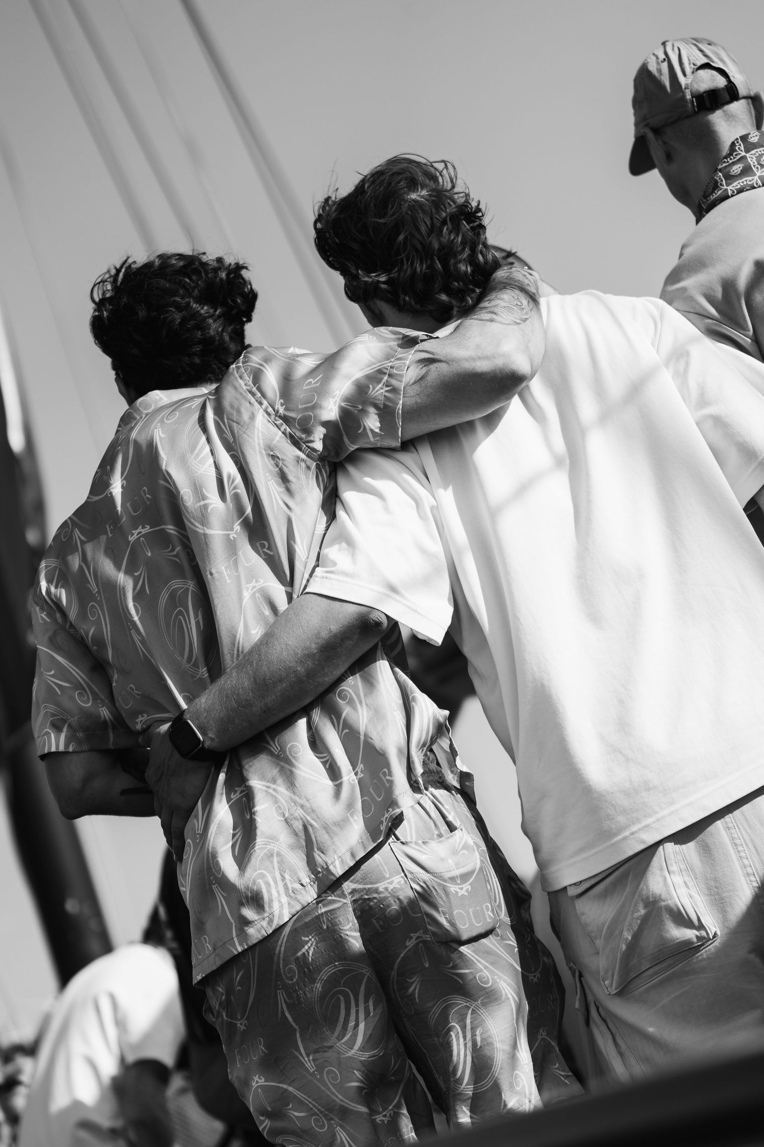 Black and white photo of two young men with arms around each other standing outdoors in casual summer shirts.
