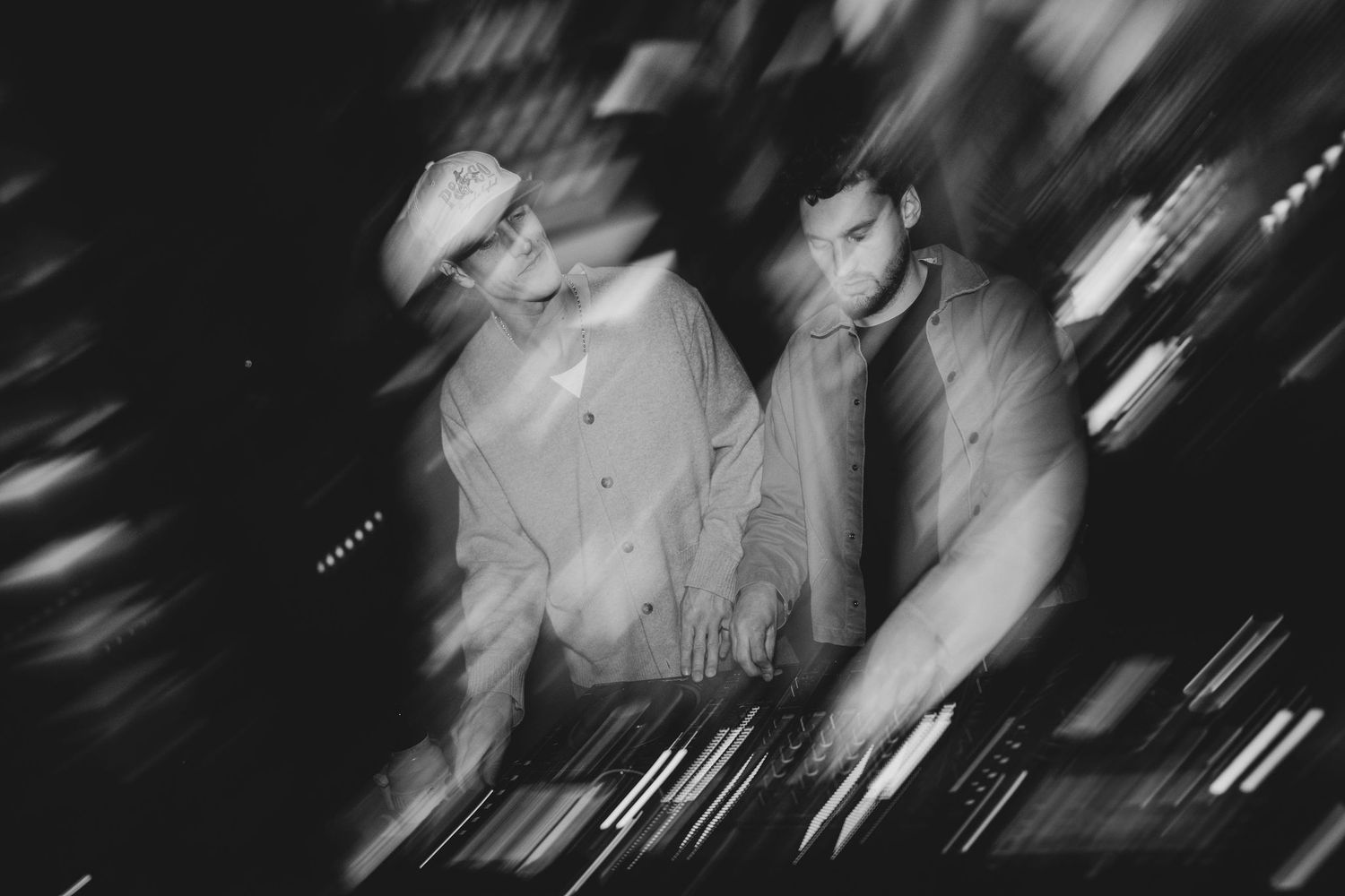 Two DJs performing at a club, captured in a blurry black and white motion shot.