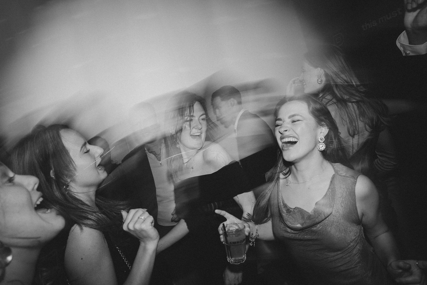 Black and white photo of joyful guests dancing and laughing energetically at a lively evening celebration.