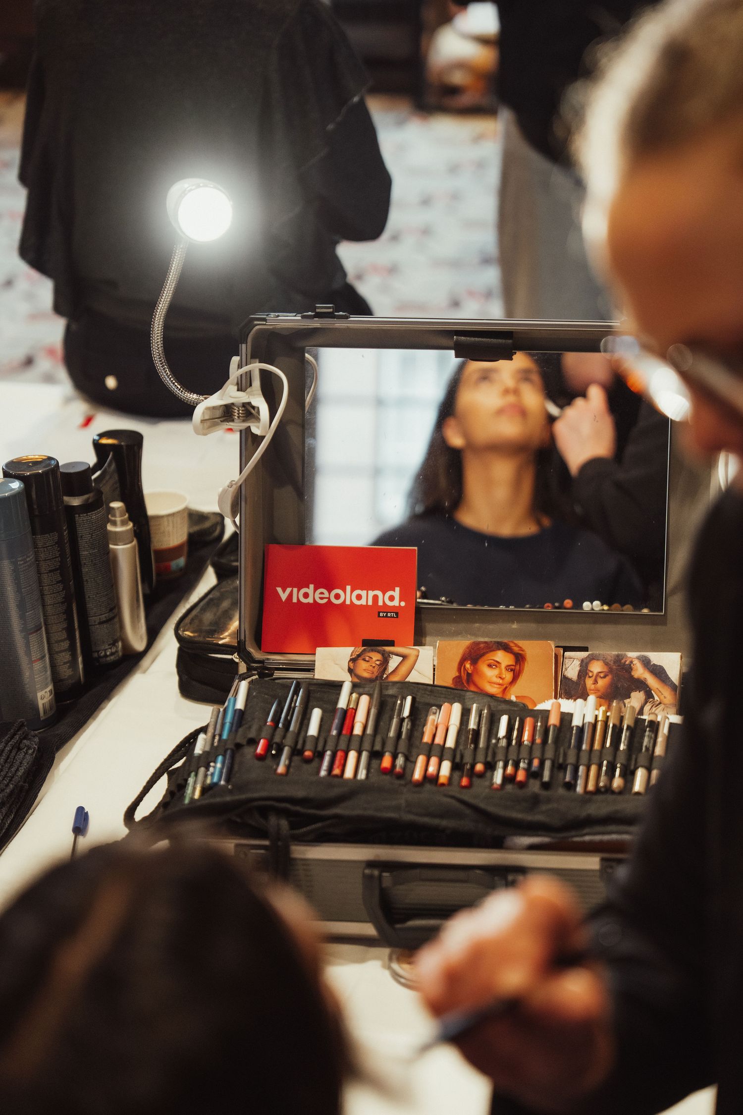 Makeup artist applying cosmetics backstage with a Videoland branded mirror and professional brush kit on a vanity table.