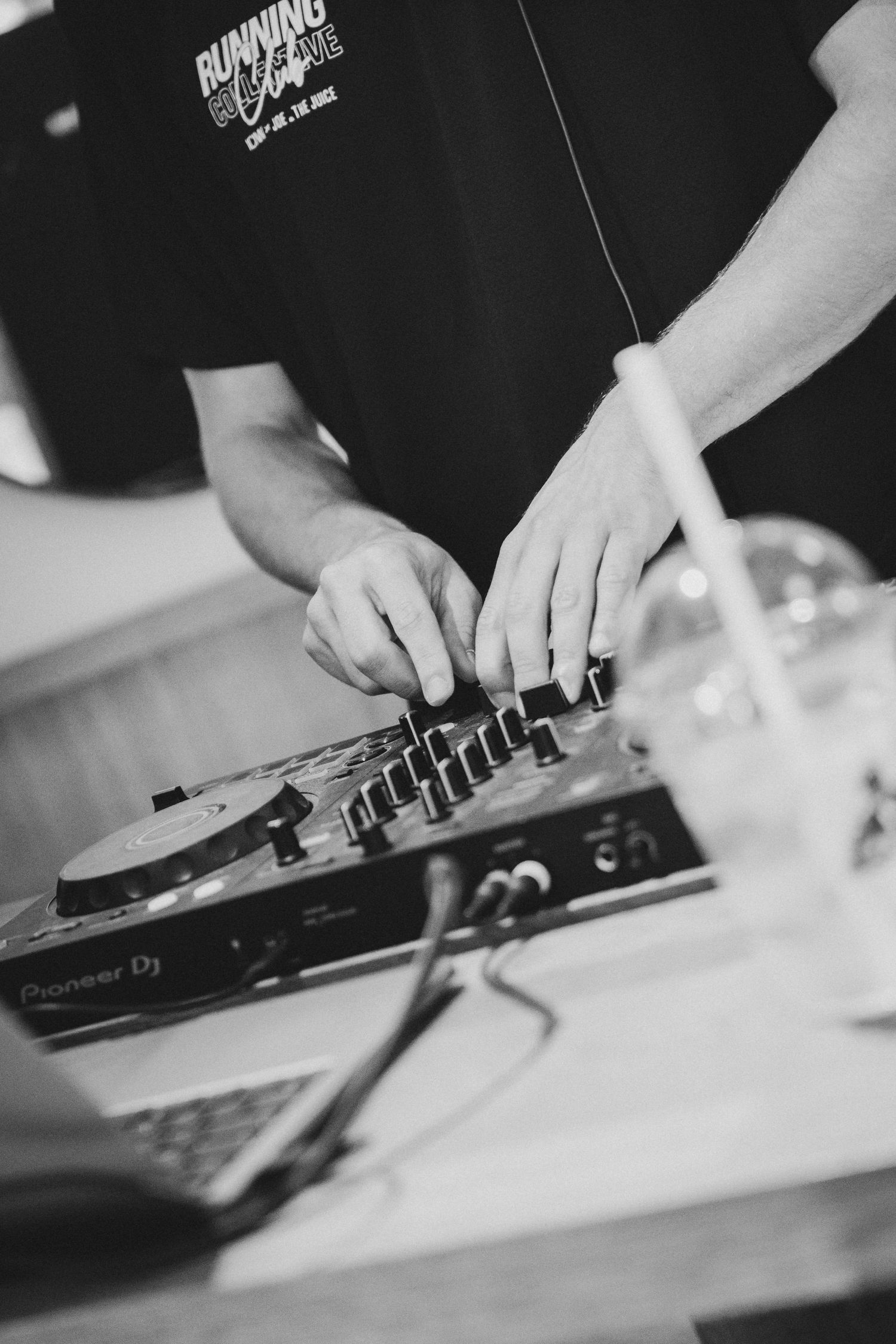 DJ mixing music on Pioneer DJ controller in black and white photo at an indoor event.