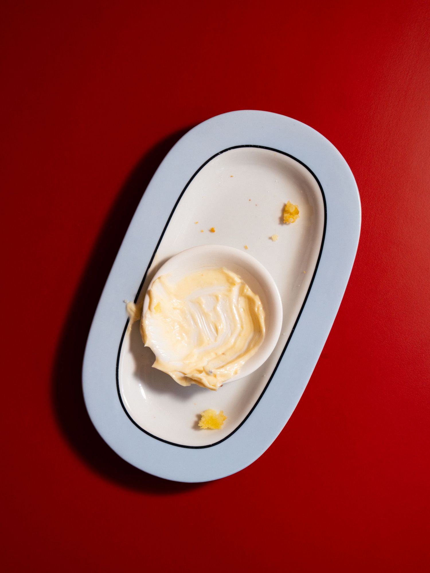 Creamy butter dessert in a white bowl on an oval plate against a bold red background.
