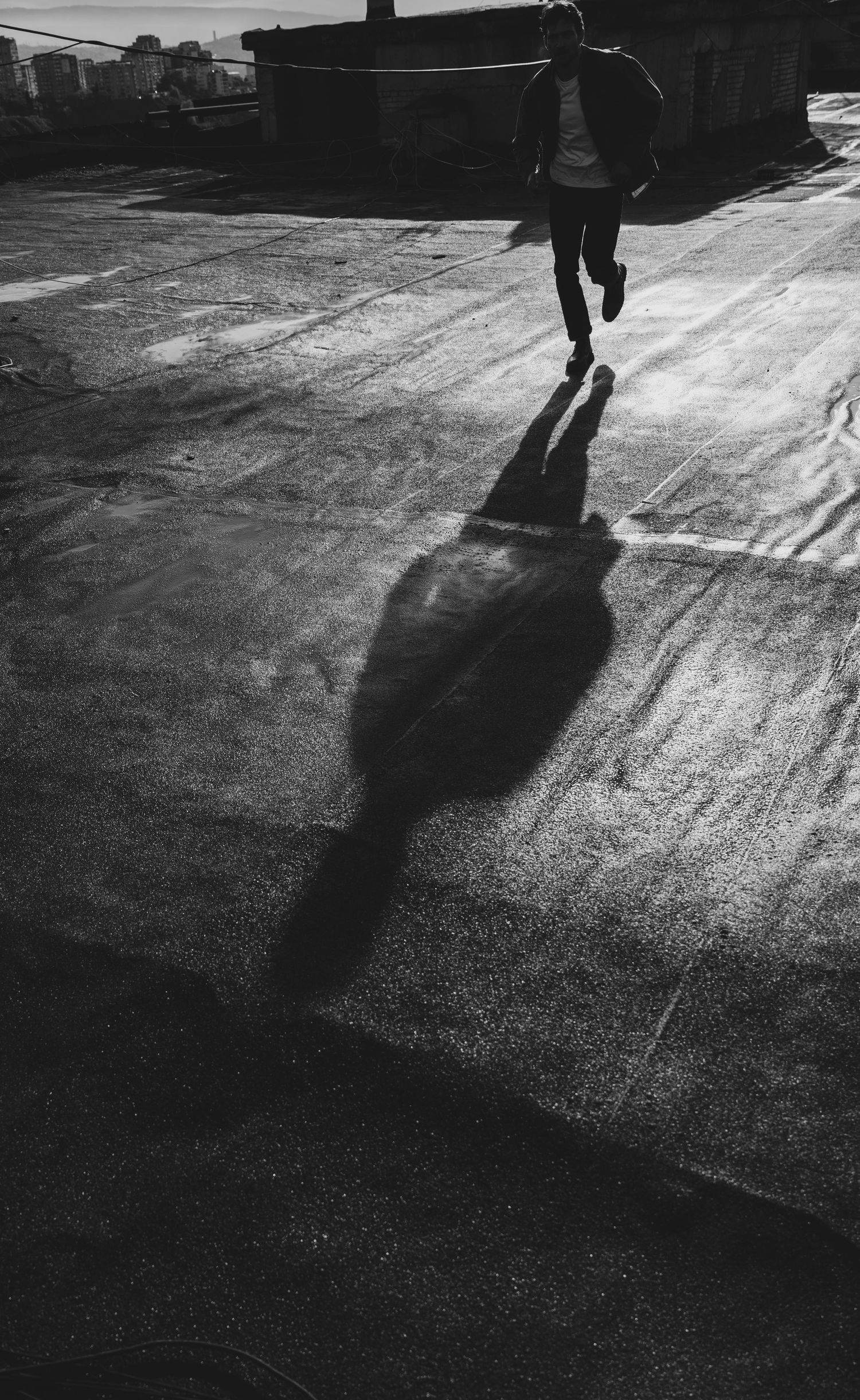 Black and white series of silhouettes walking across a wet pavement casting long dramatic shadows in low light.