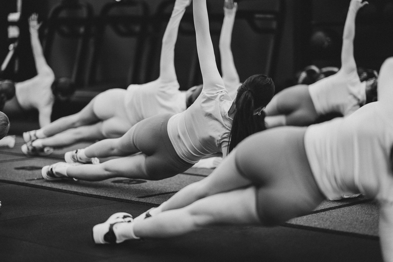 Group fitness class performing side-lying stretches on mats in a gym, black and white photo.