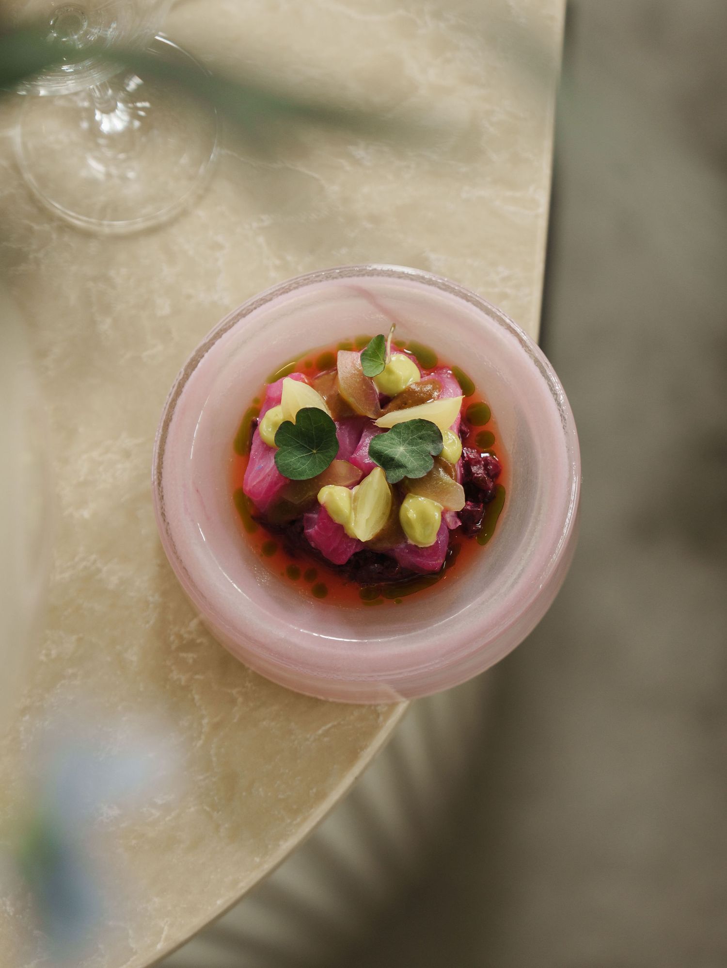 Elegant pink bowl with gourmet dish featuring pickled vegetables, herbs, and colorful garnishes on a marble surface.
