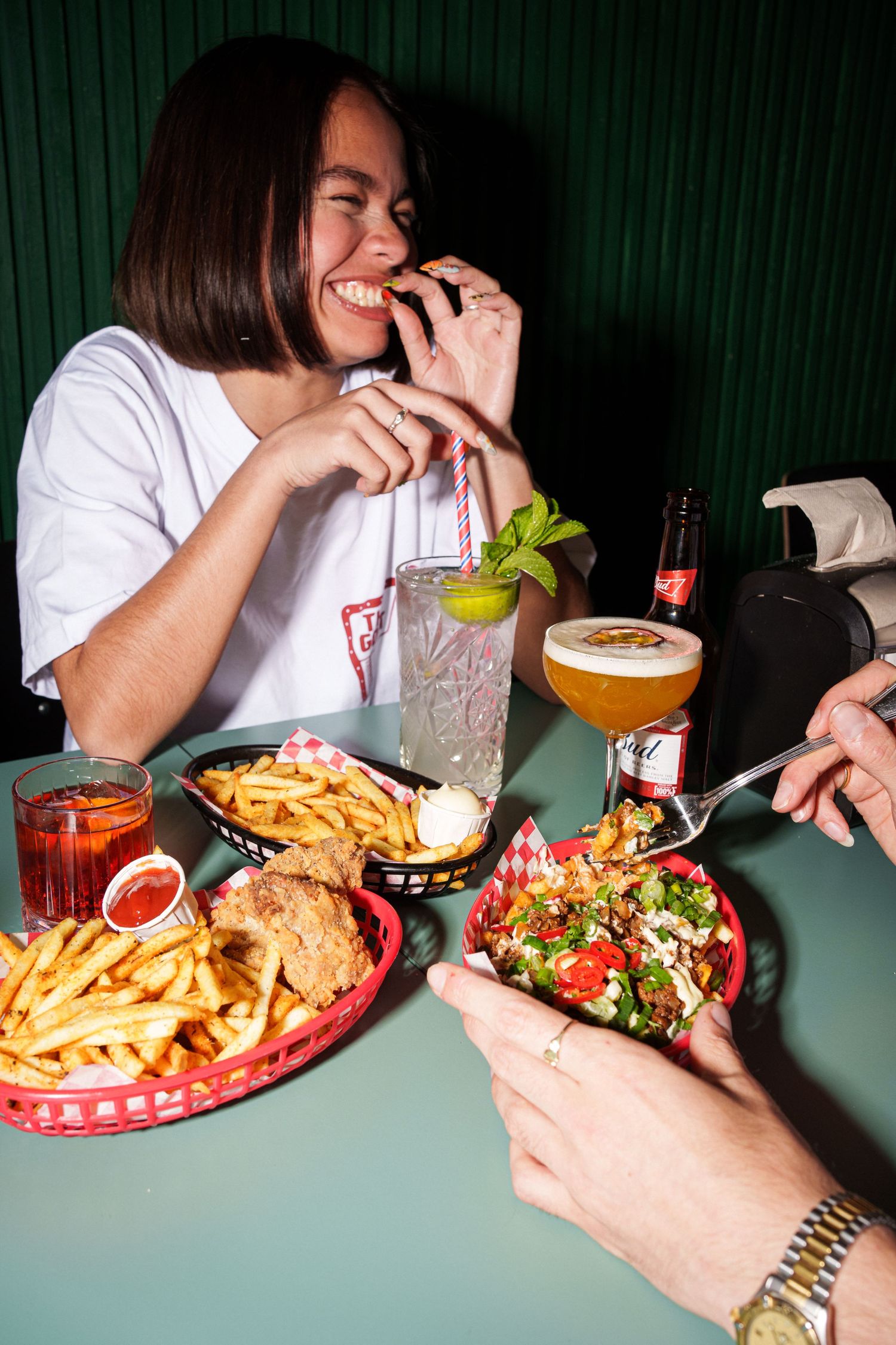 Woman laughing while eating a burger with fries, salad, and drinks at a retro diner booth.