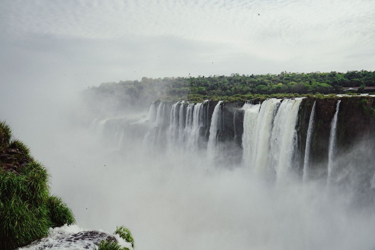 Panoramic view of Iguazu Falls with massive cascading waterfalls surrounded by lush green tropical forest and mist.