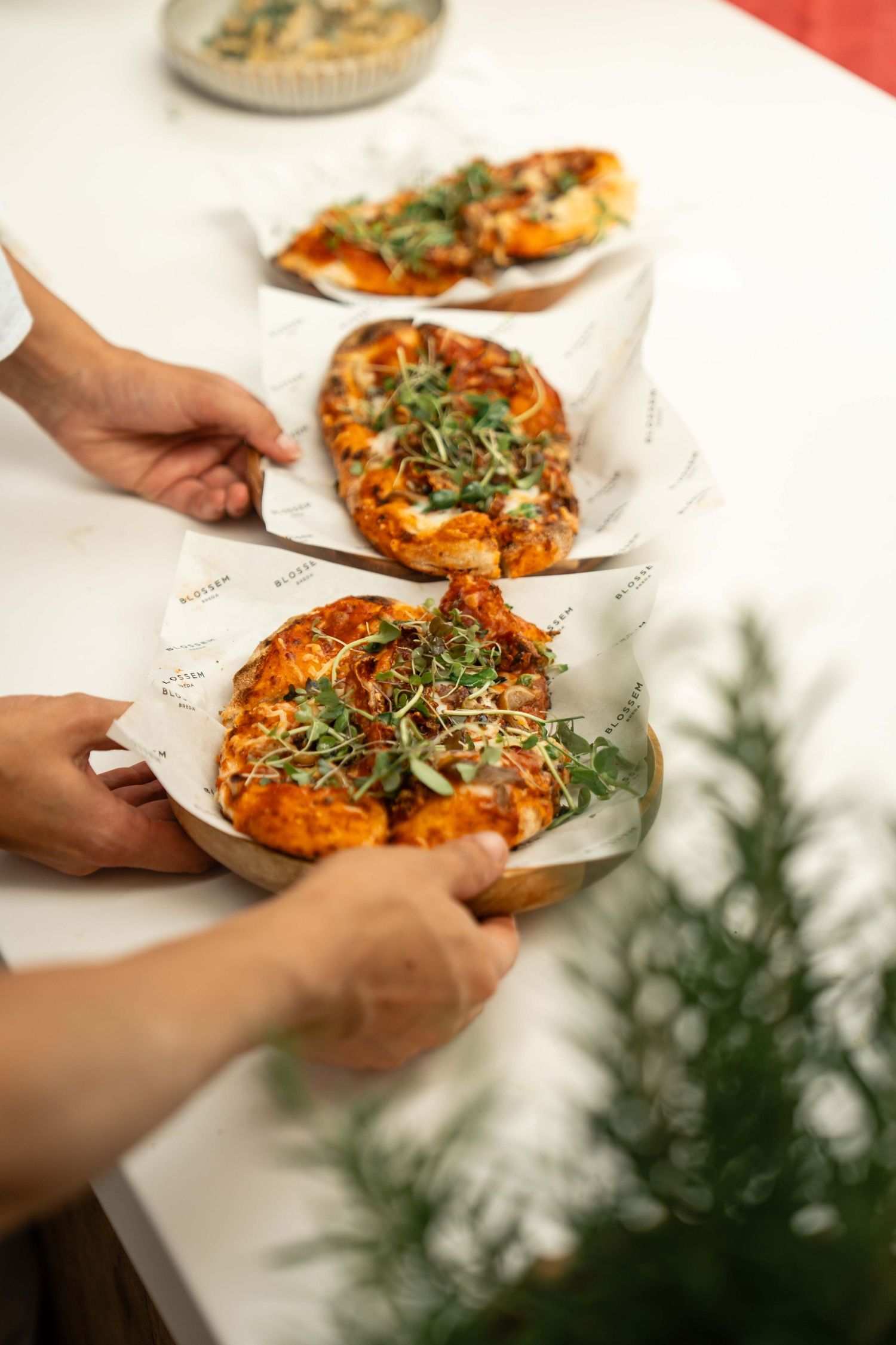 Hands serving personal flatbread pizzas topped with fresh microgreens and tomato sauce on wooden boards.