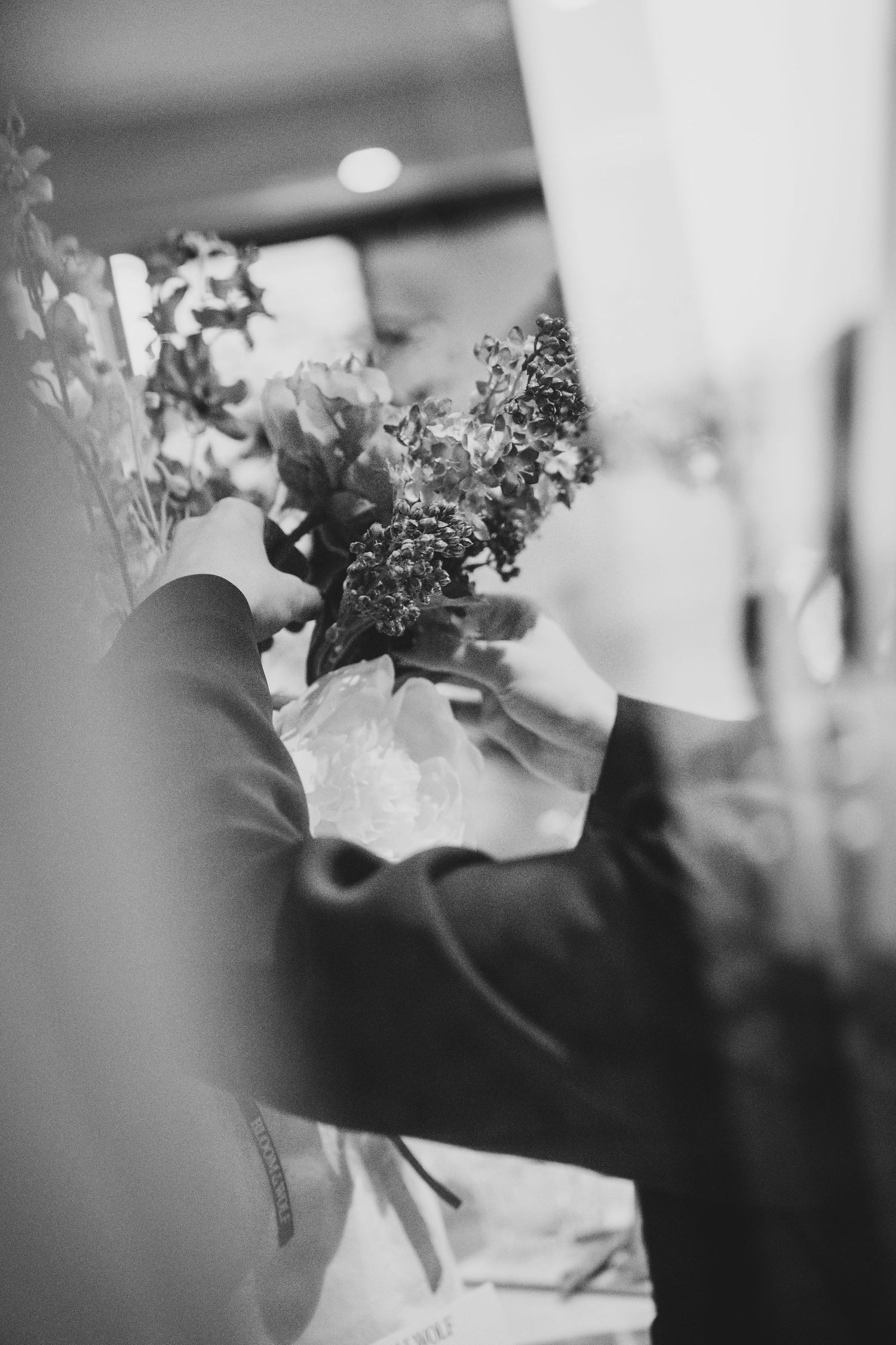 Black and white photo of hands arranging a floral bouquet with greenery at a wedding ceremony.