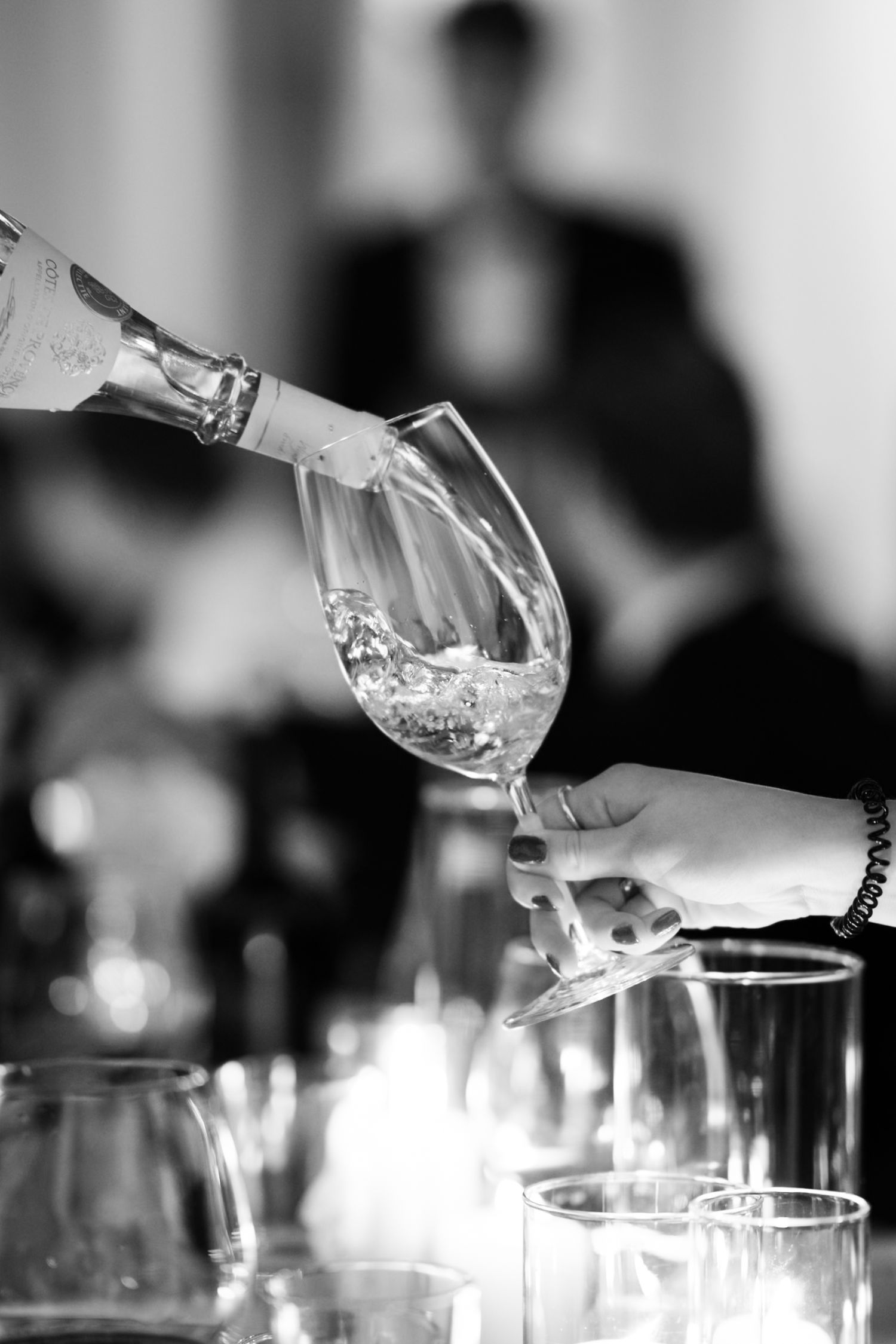 Black and white photo of wine being poured into a crystal glass held by a hand at an elegant event.