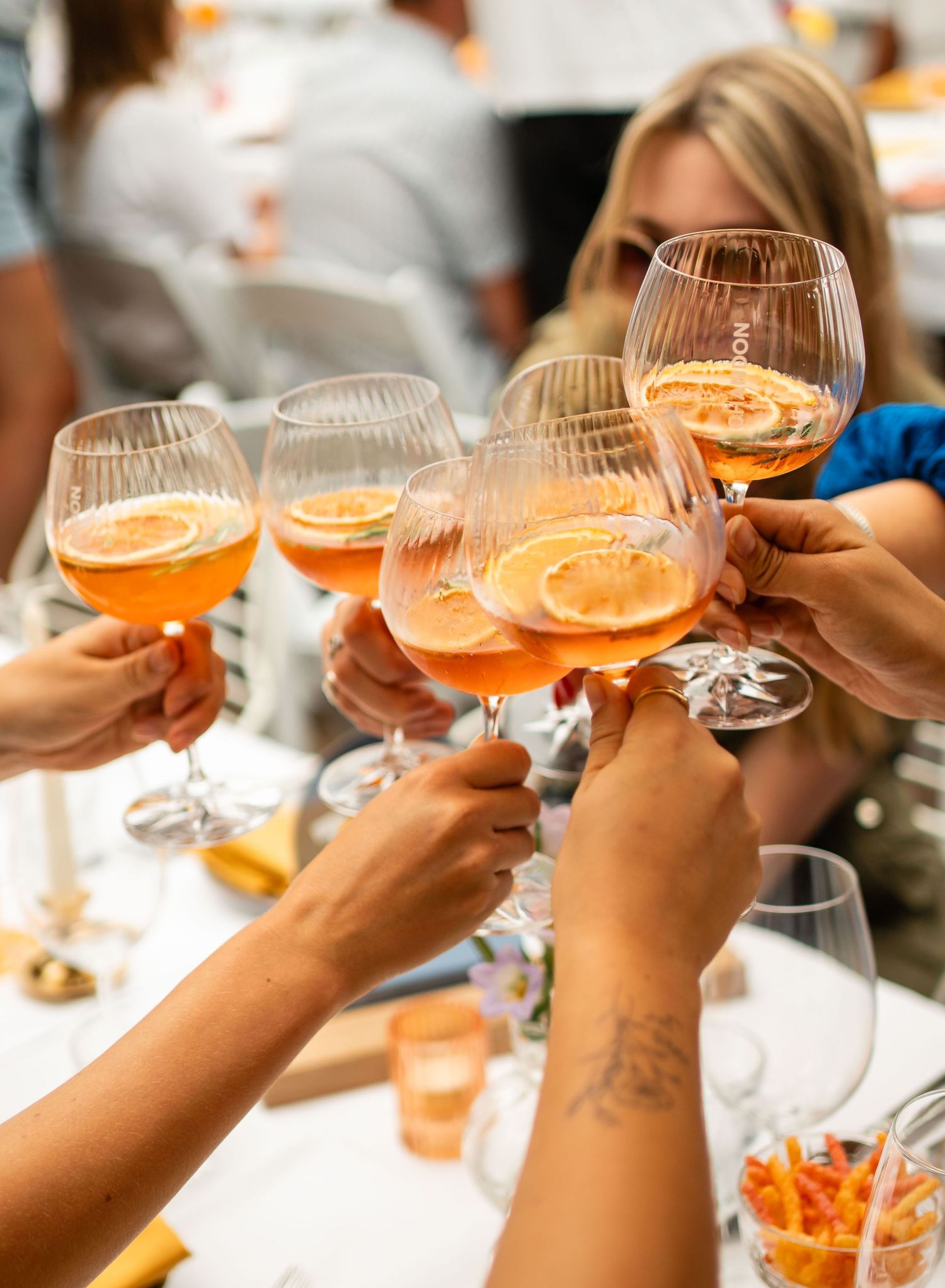 Group of friends toasting with orange Aperol Spritz cocktails garnished with lemon slices at a social gathering.