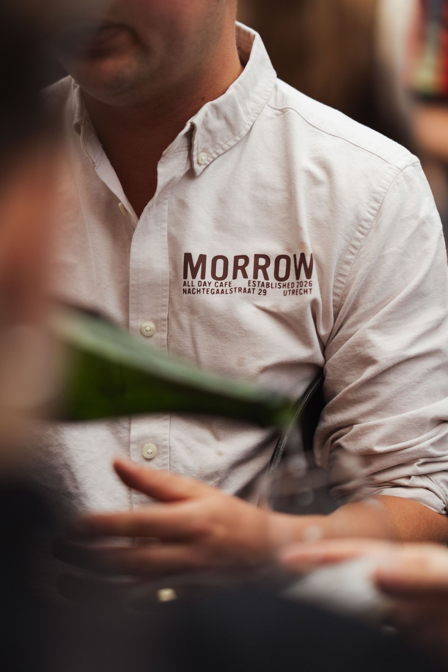 Man wearing a white Morrow All Day Cafe Utrecht branded button-up shirt at a casual dining event.