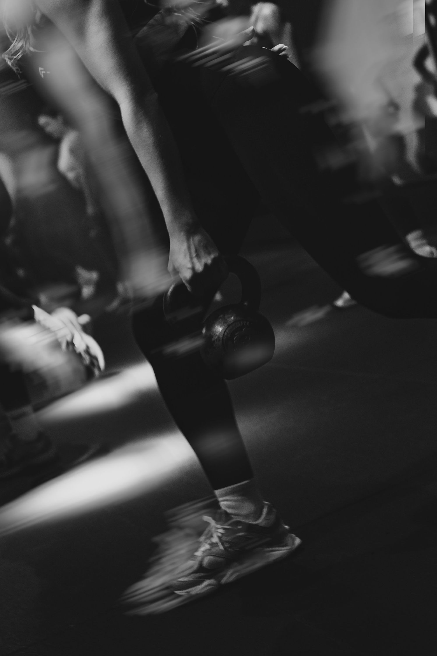 Black and white motion blur photo of people exercising with kettlebells in a dynamic fitness class.