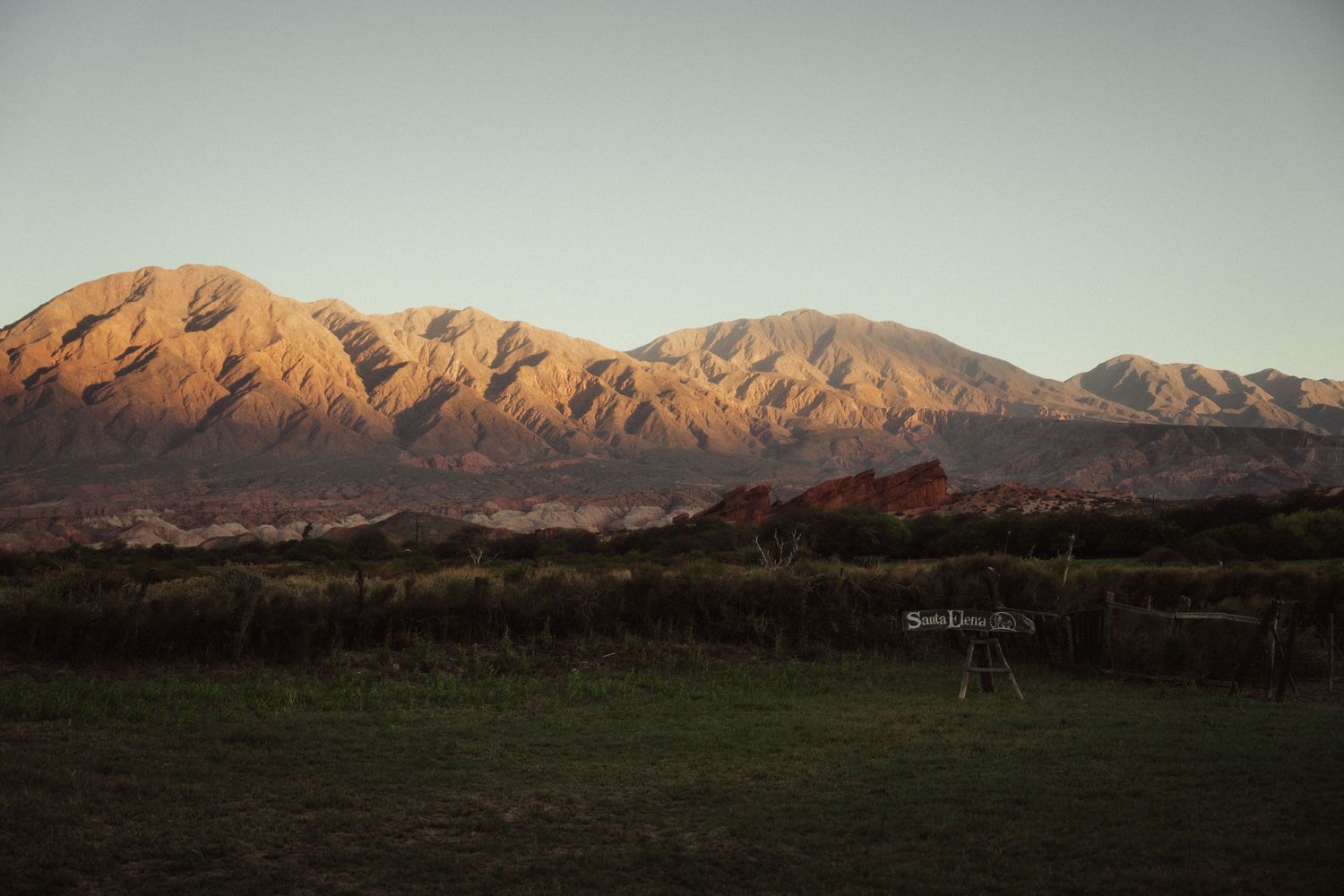 Mountain range glows orange and purple during sunset against a desert landscape.