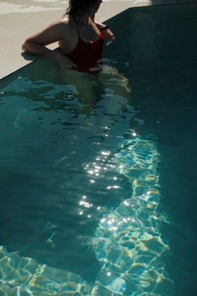 Woman in red swimsuit standing in a sparkling turquoise swimming pool on a sunny day.