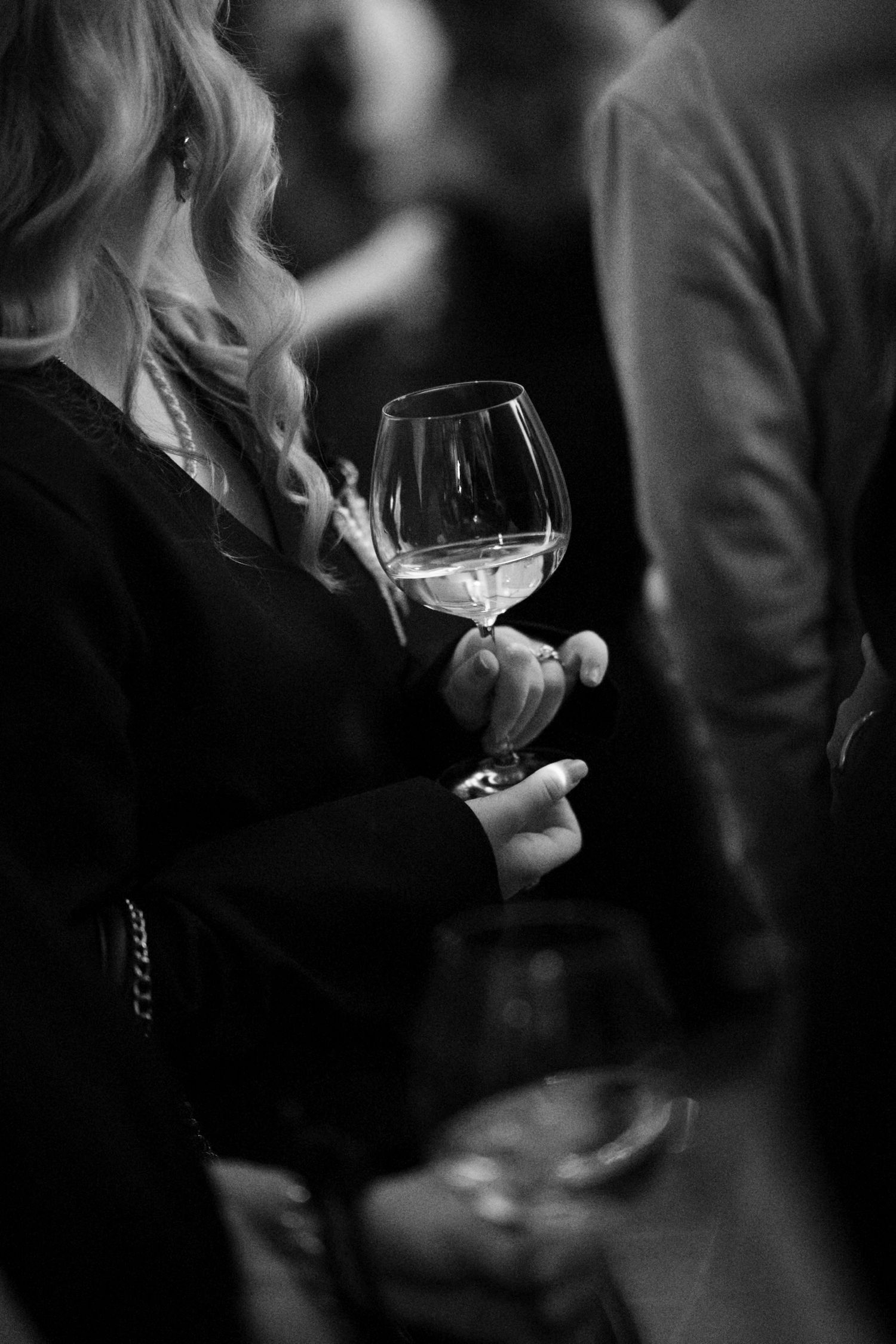 Black and white photo of a woman in a black dress holding a wine glass at an elegant social event.