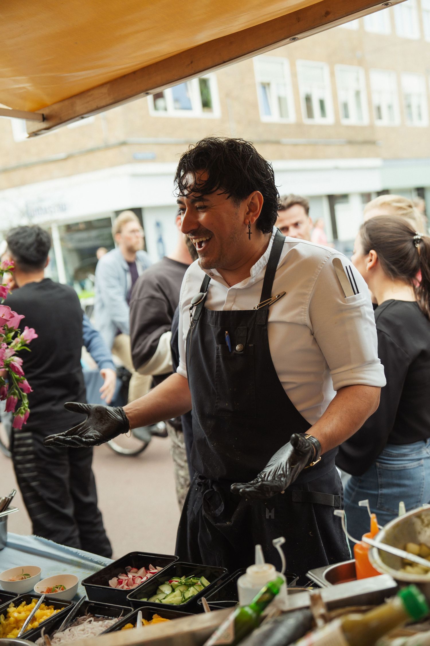 Smiling chef in black apron and gloves serving food at an outdoor street market stall.
