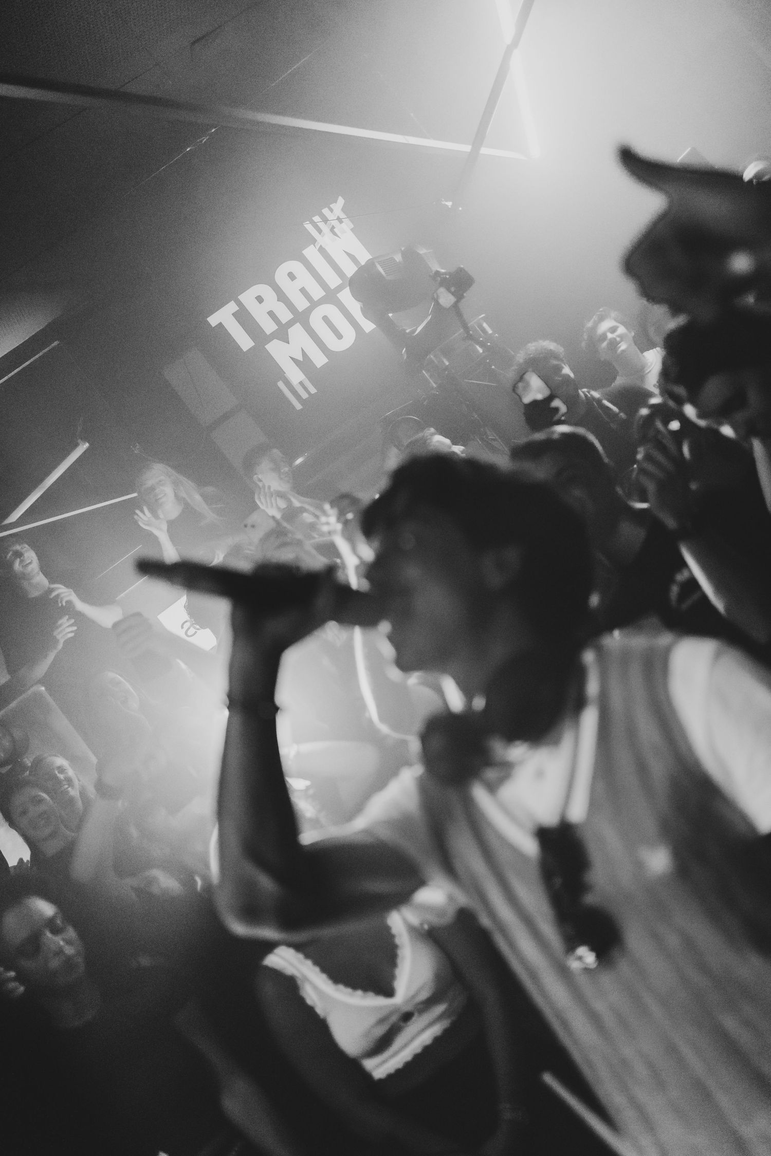 Black and white photo of a rapper performing on stage with microphone before an energetic crowd.
