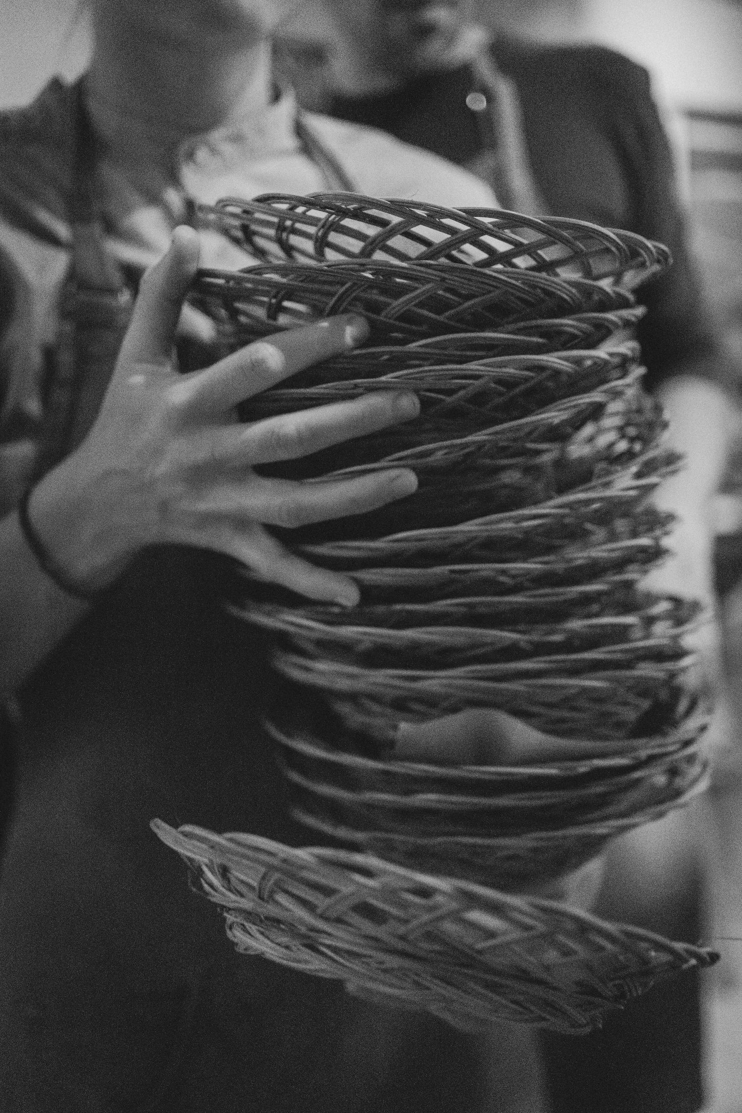 Black and white photo of hands holding a stack of woven wicker baskets.